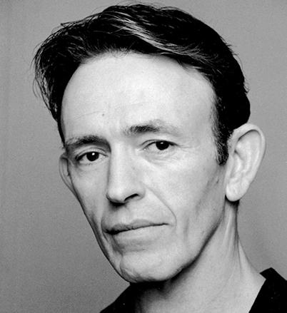 A headshot of a man in black & white. He is wearing a black shirt.