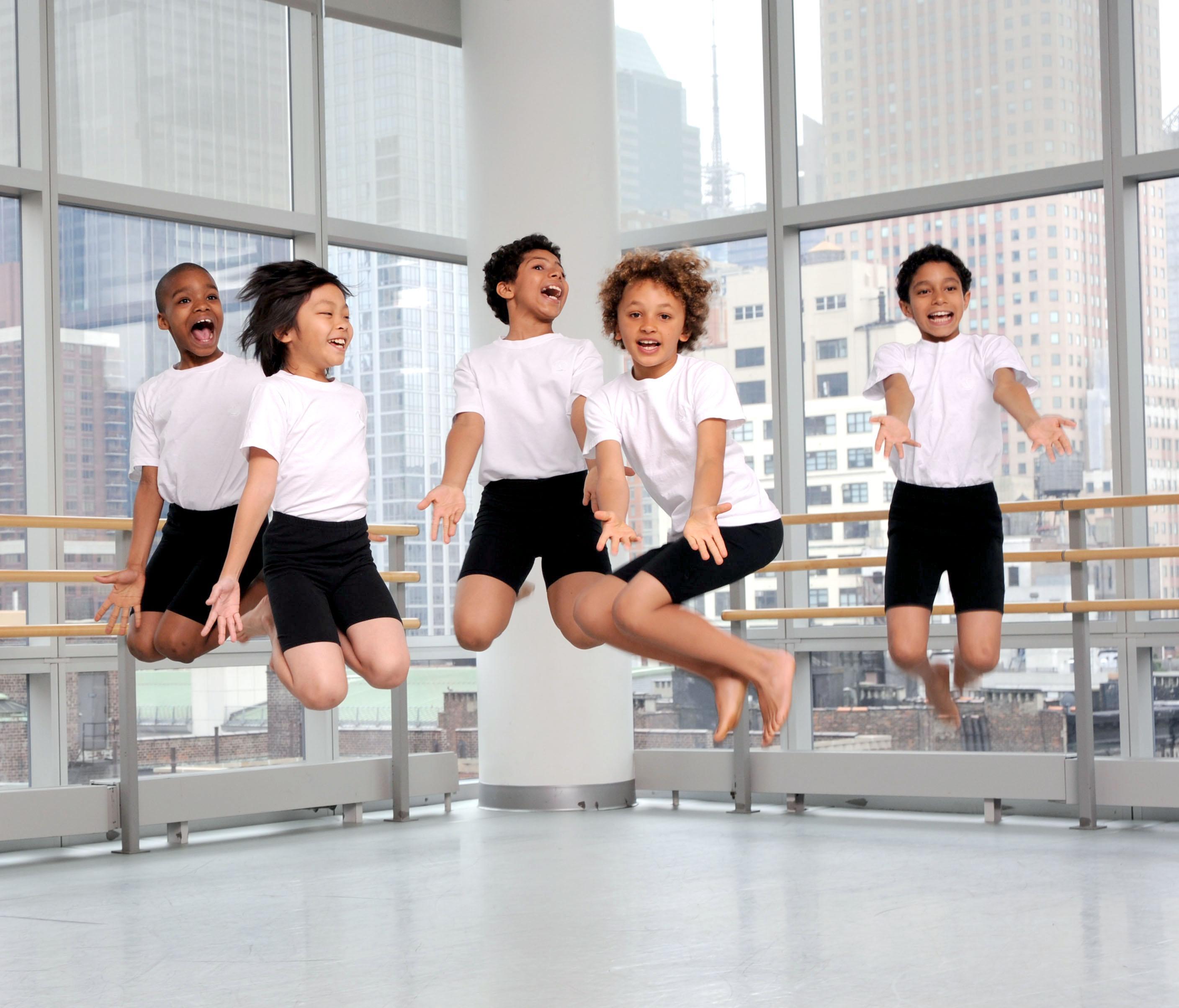 5 boys in white shirts and black shorts jump in a dance studio