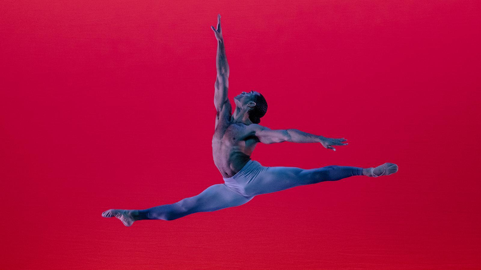 A color photo of James Gilmer performing in Alvin Ailey's The River, captured by Paul Kolnik. Gilmer is mid-leap with his arms and legs extended, showcasing his strength and grace, against a vibrant red background.