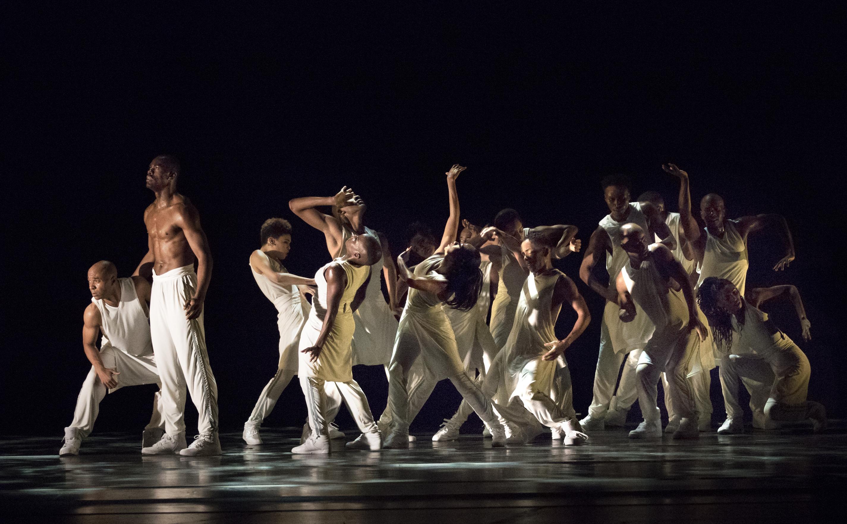 A group of dimly lit dancers wearing white and striking poses