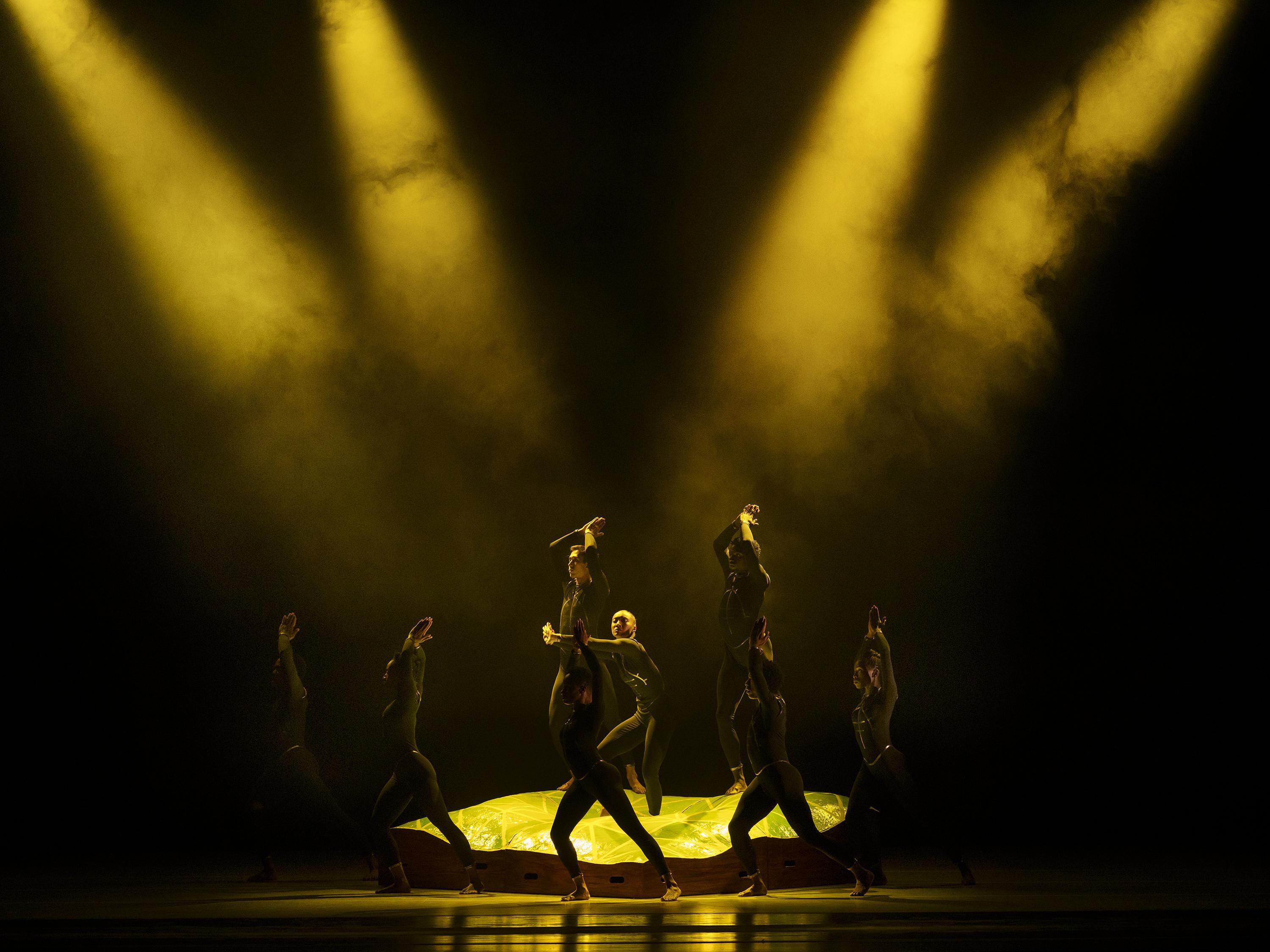 Dancers on stage with four yellow lights shining down on them.