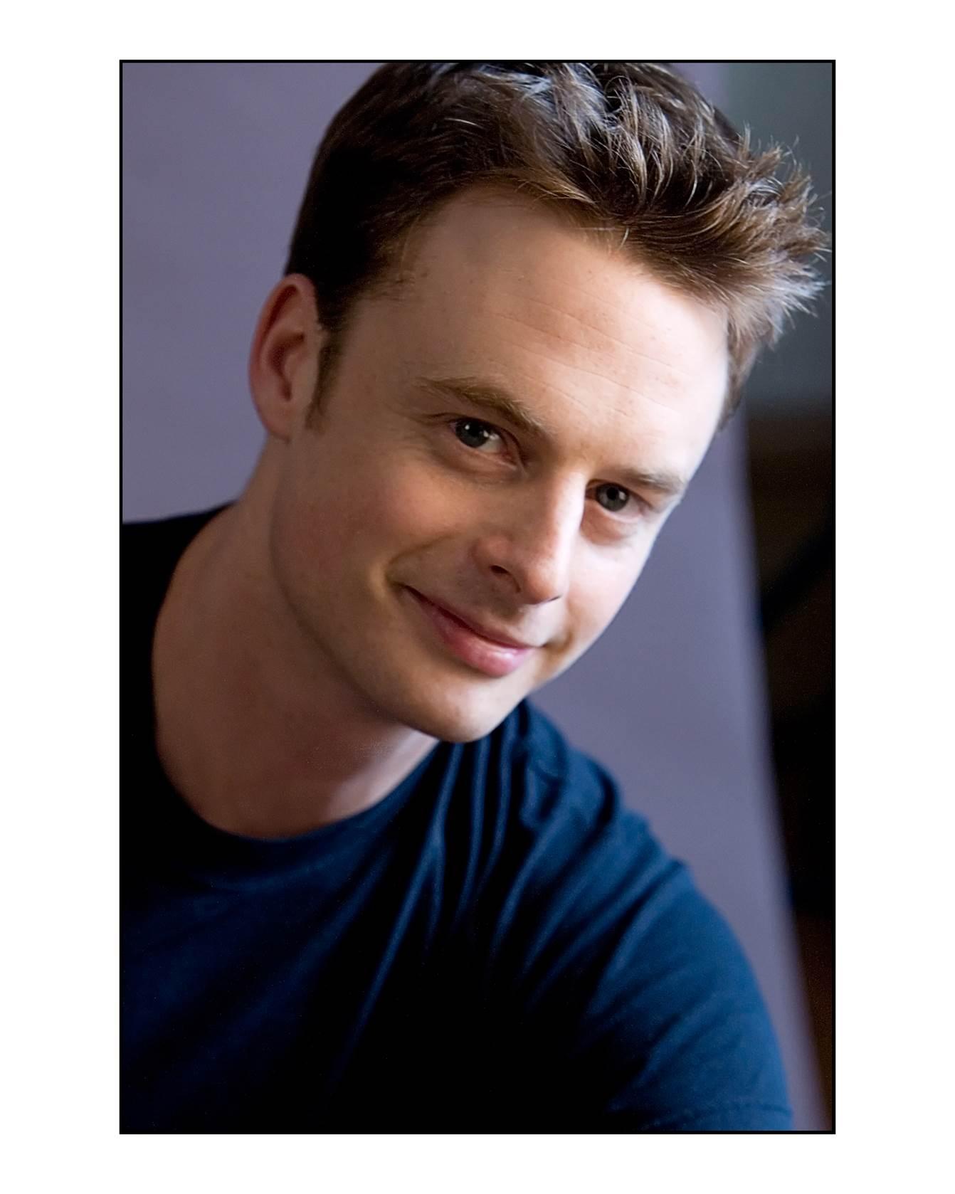 A man's headshot. He has spiky hair and is wearing a navy shirt.