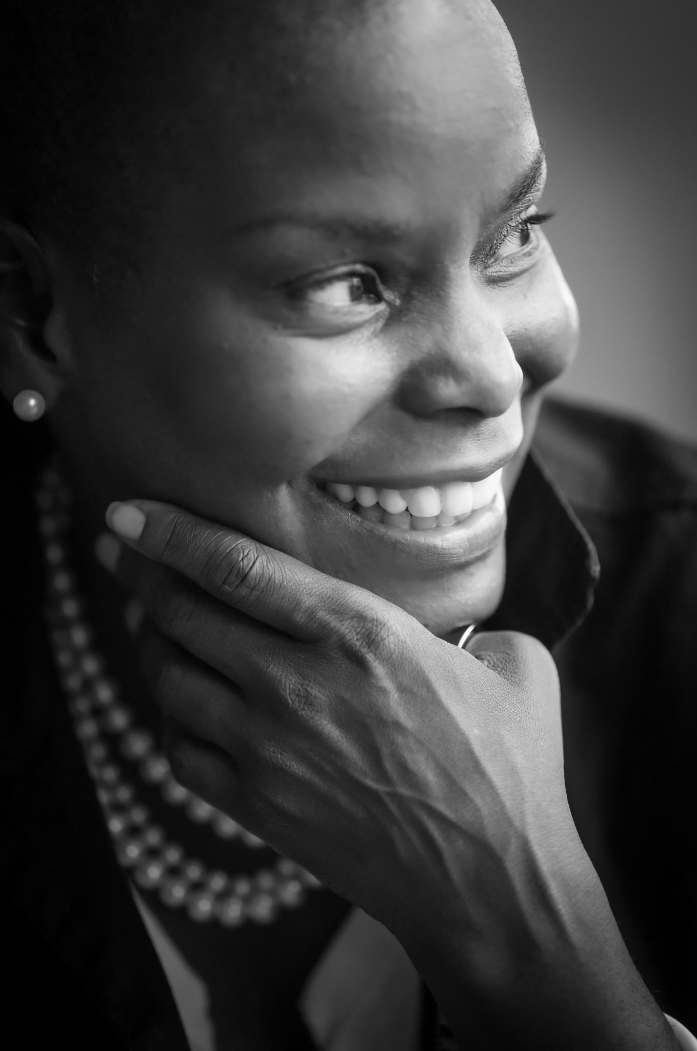 A black woman looks off to the right smiling. She has her hand resting on her chin.