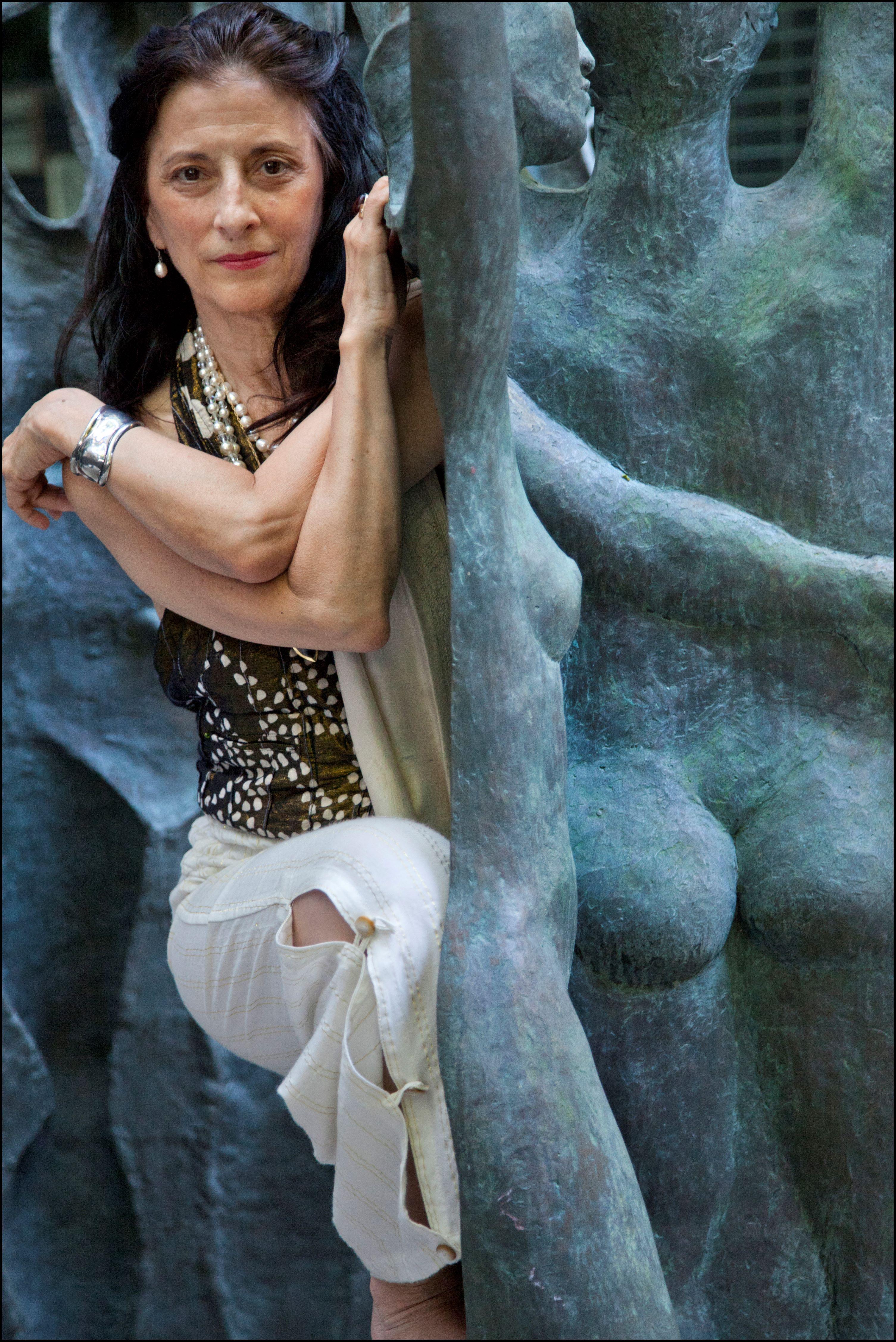 A woman sits within a rock sculpture. She is wearing white pants and a green tank top. Her arms are crossed