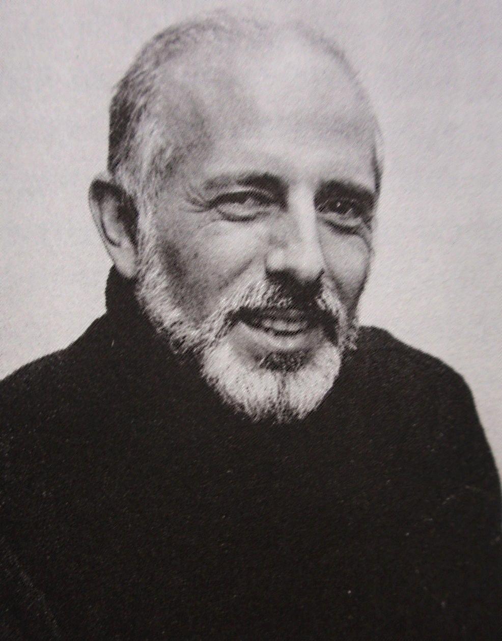 A white haired man is wearing a black turtleneck. The photo is in black and white. He has a goatee.