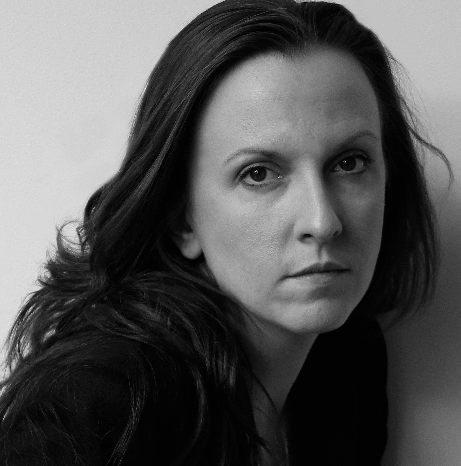 A black and white headshot of a woman with long hair and a black top.