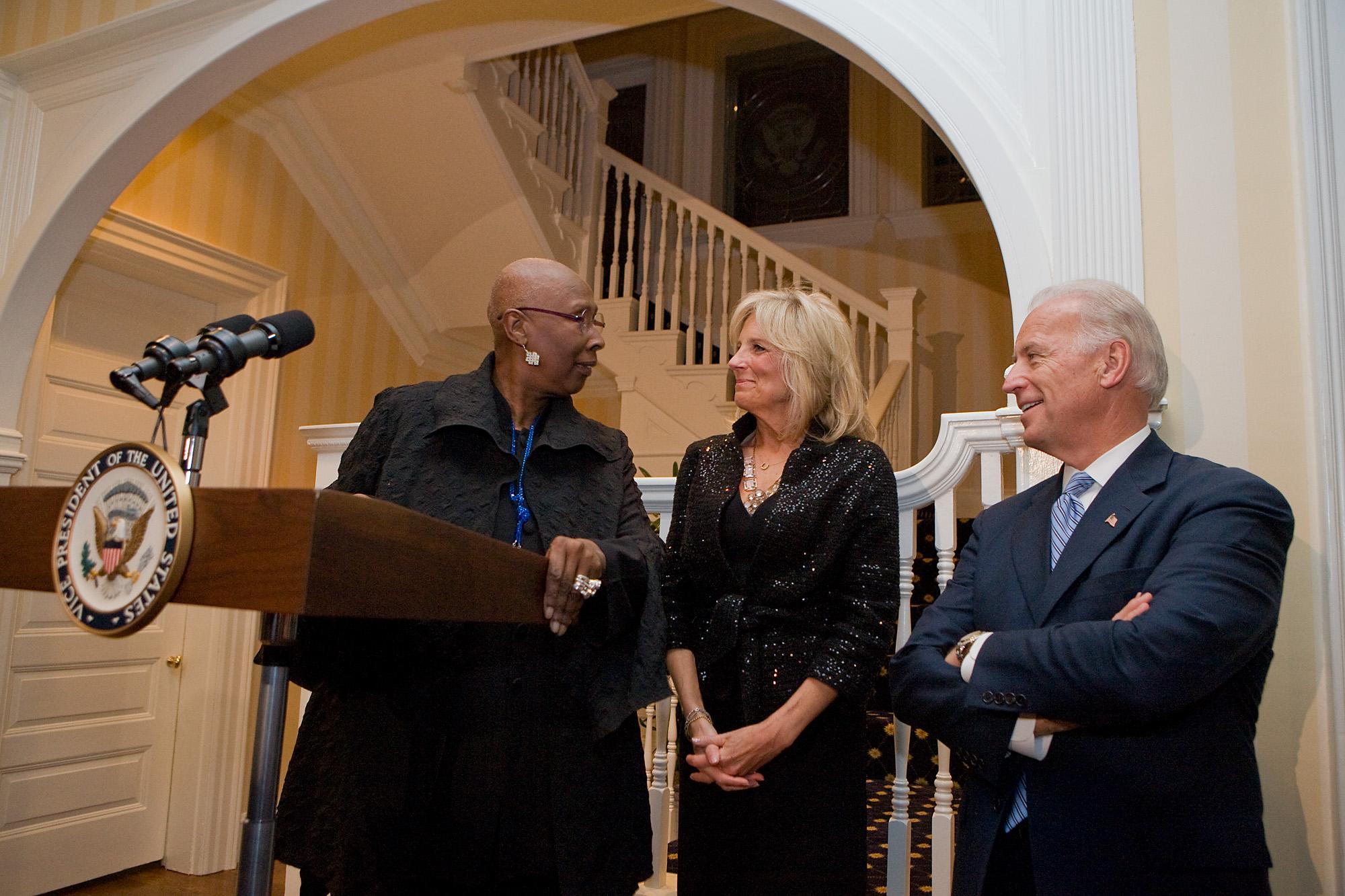 Judith Jamison, Artistic Director of AAADT, speaking at a podium with the Vice President's seal. She is joined by Dr. Jill Biden and Vice President Joe Biden at a reception for the dance company, held at the Naval Observatory. The three are smiling and engaged in conversation. The setting is a formal room with a staircase in the background. Photo by David Lienemann, 2010.