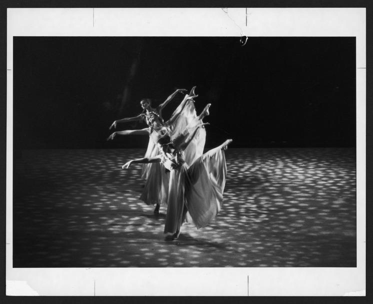 In this 1982 photograph, dancers Mari Kajiwara, Donna Wood, and Maxine Sherman are performing Alvin Ailey's "Satyriade." The image captures the dancers in mid-movement, each extending an arm gracefully as their flowing costumes create a sense of fluidity and motion. The stage is bathed in a patterned light that adds depth and texture to the scene. The composition of the photograph emphasizes the synchronization and harmony of the dancers, highlighting the elegance and precision that Alvin Ailey's choreograp