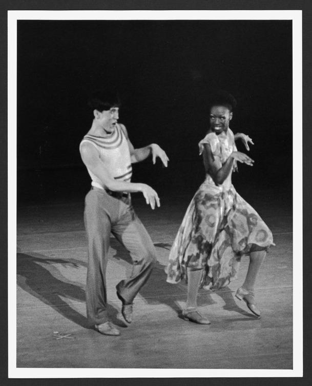 This photograph from 1981 captures Masazumi Chaya and Marilyn Banks performing in Alvin Ailey's "Phases." The image, taken by Jack L. Vartoogian, showcases a dynamic moment in their dance, with both dancers adopting expressive, playful poses. Chaya, dressed in a sleeveless top and pants, and Banks, in a flowing dress, appear to be fully engaged in their roles, exuding energy and character. Their expressions and body language convey a sense of joy and connection, highlighting the lively and emotive nature of