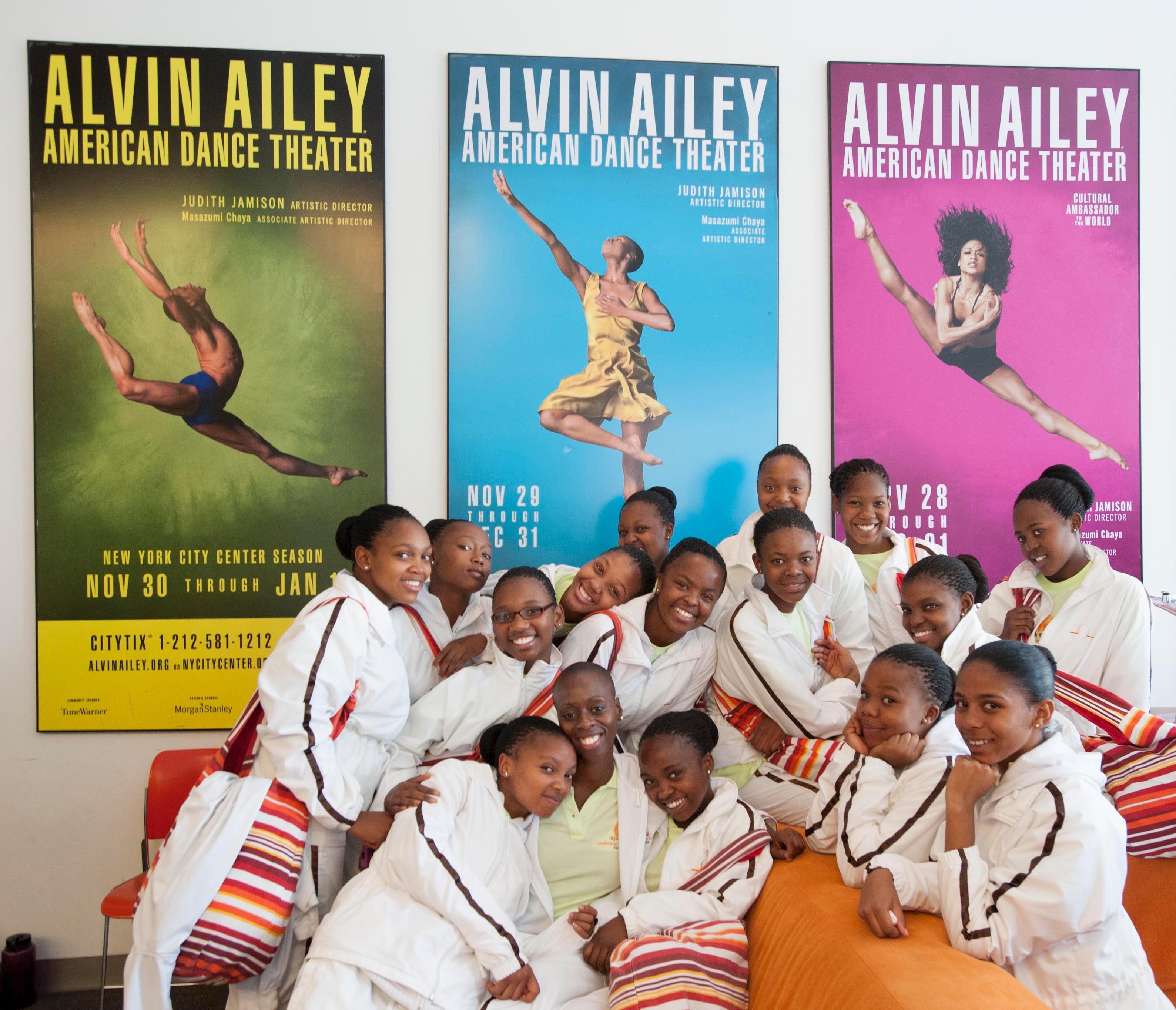 Group of dancers in white track suits standing in front of AILEY posters