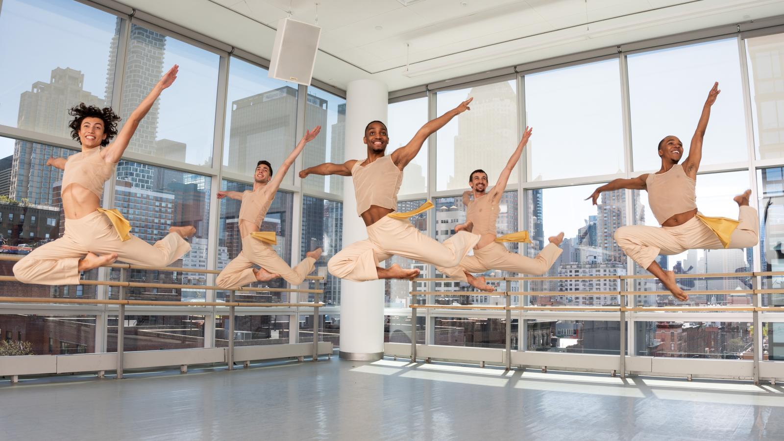 Six students in beige costumes leap in a dance studio