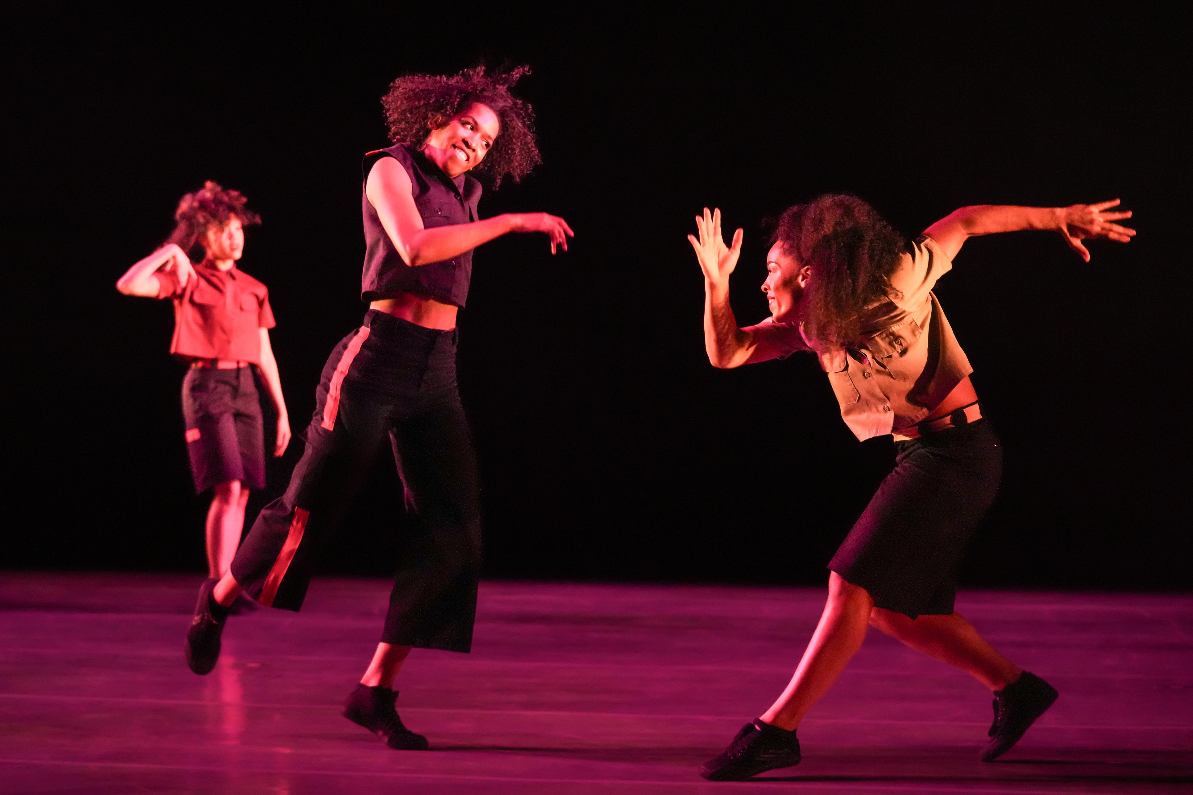 Three dancers move on stage wearing black shorts and light color tops,