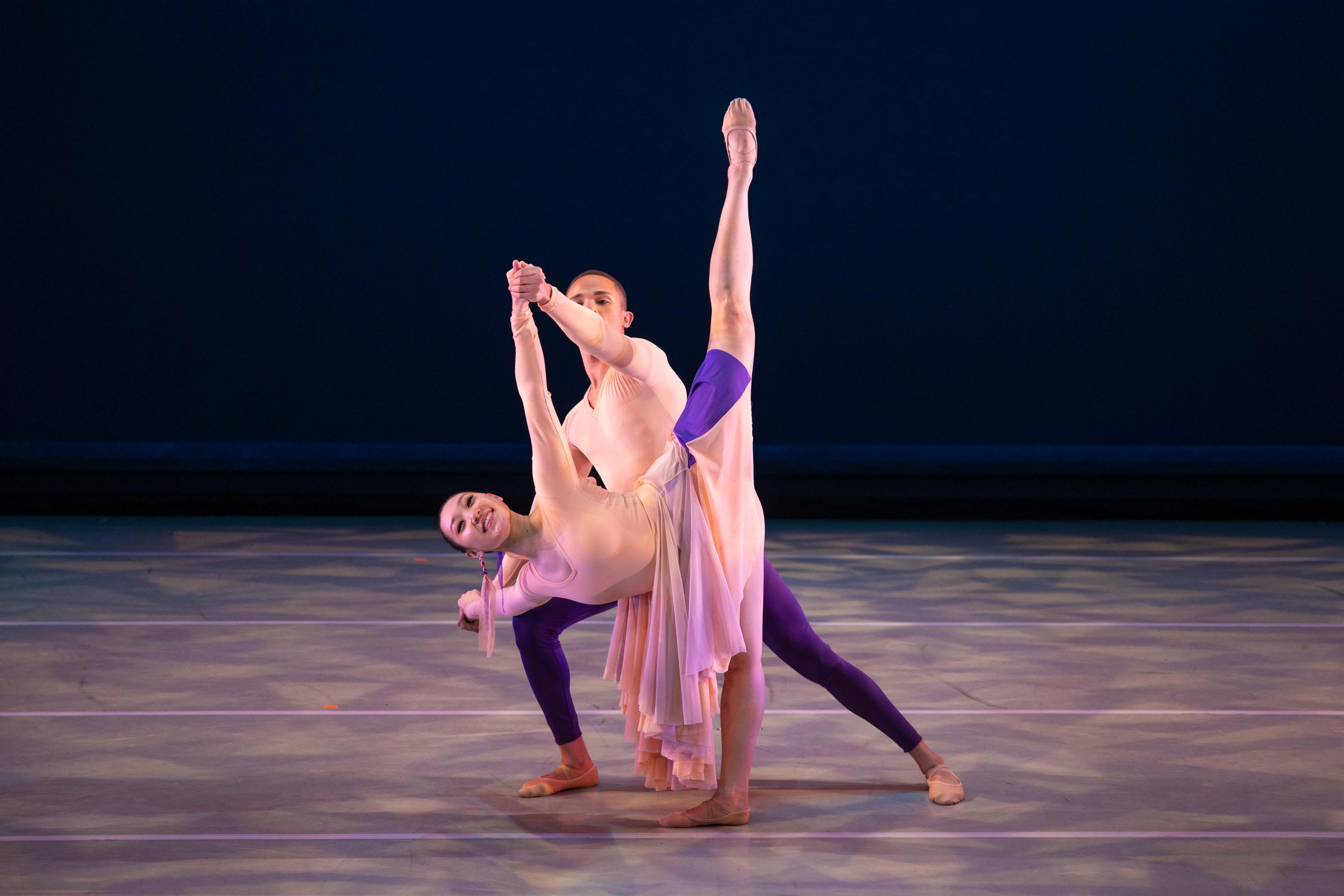 A man stands behind a woman who is bending to the side with her leg up in the air.