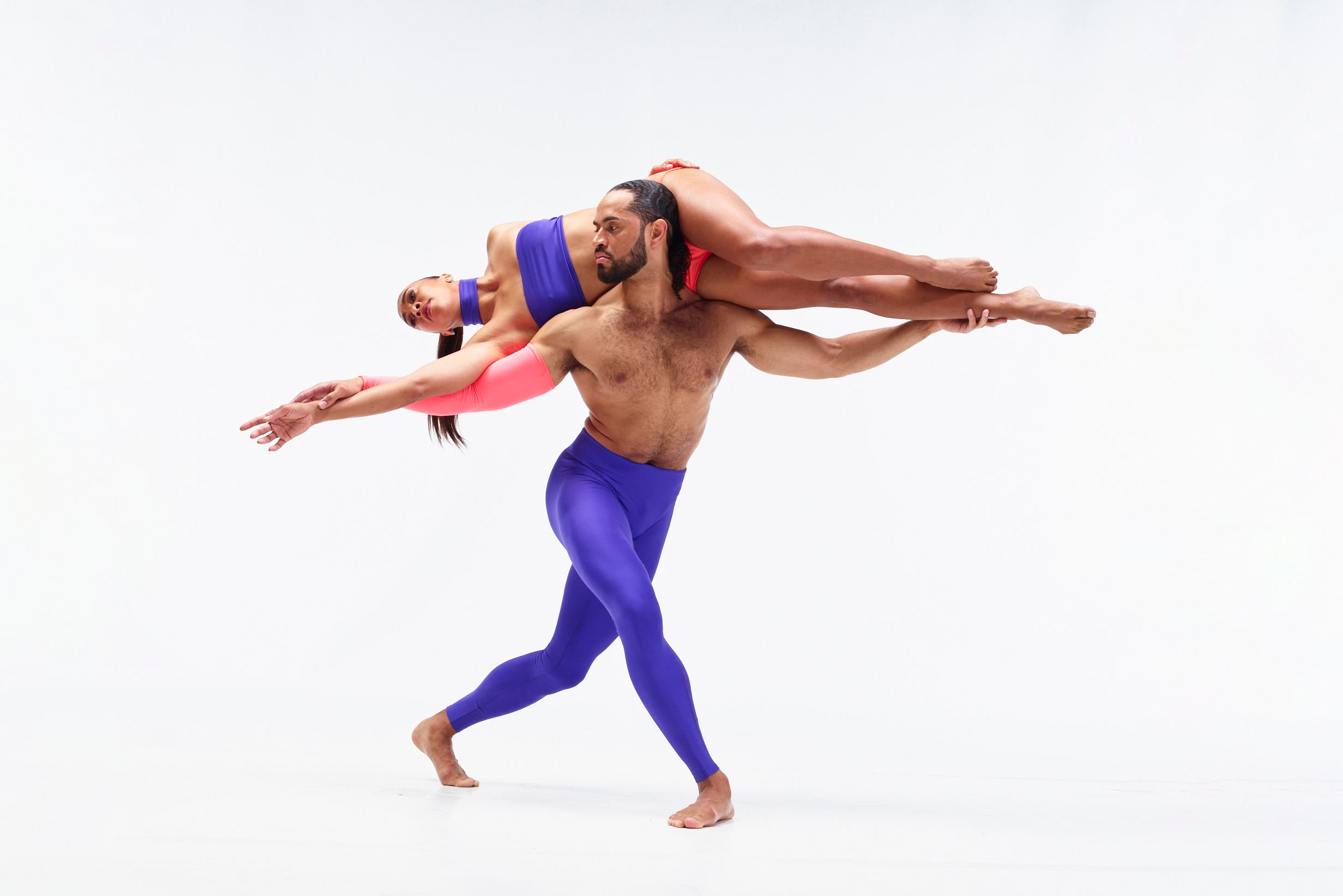 a male dancer stands with a female dancer laying sideways across his upper back