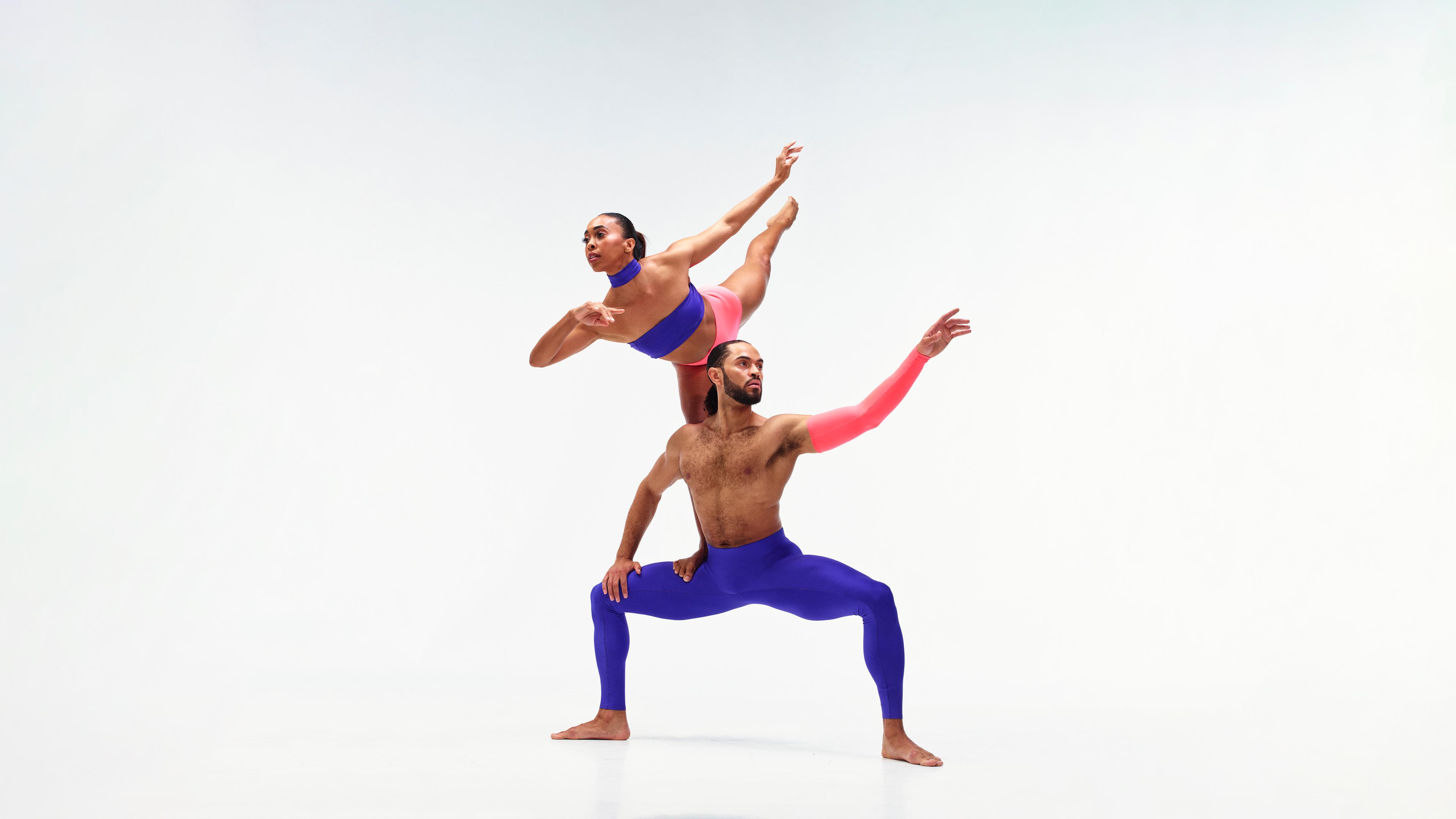 A female dancer is perched on the shoulders of a male dancer who stands with his legs bent