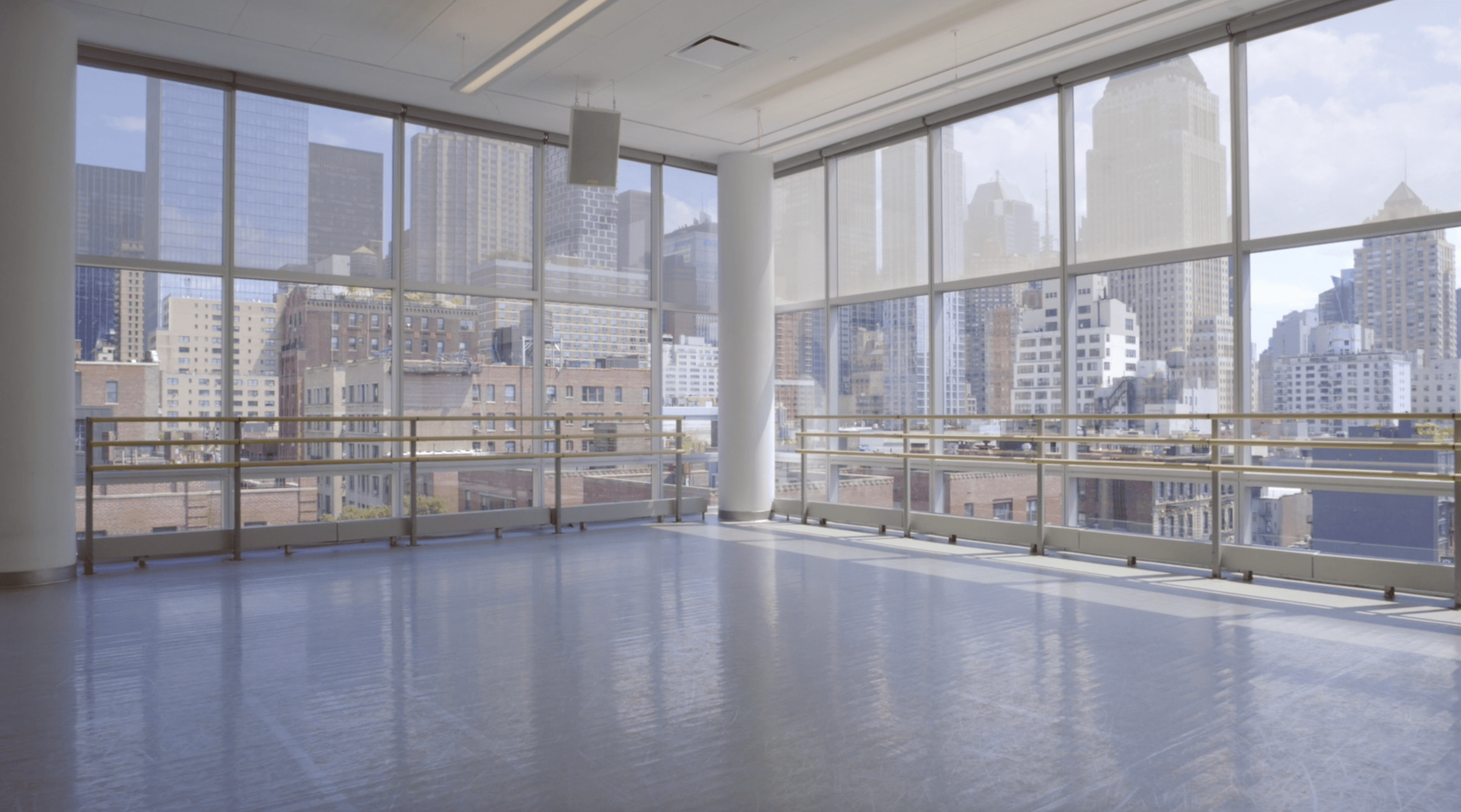 the corner of a dance studio with floor to ceiling windows and ballet barres around the perimeter