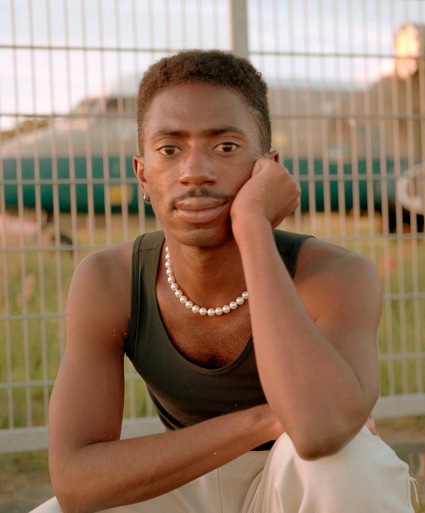 A headshot of a black man sitting with one arm on his cheek