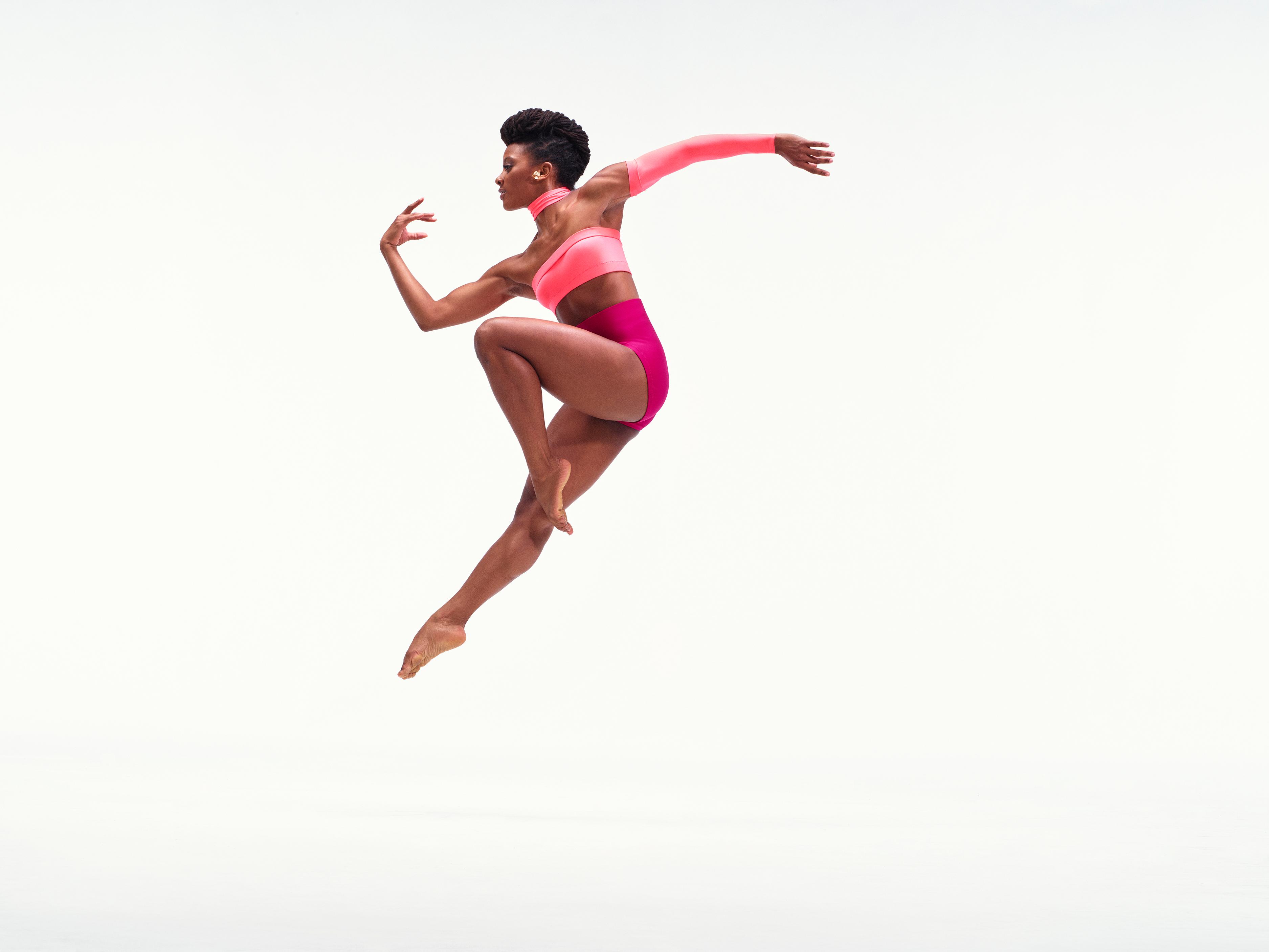 A dancer in a light pink tube tob and dark pink shorts jumps in the air