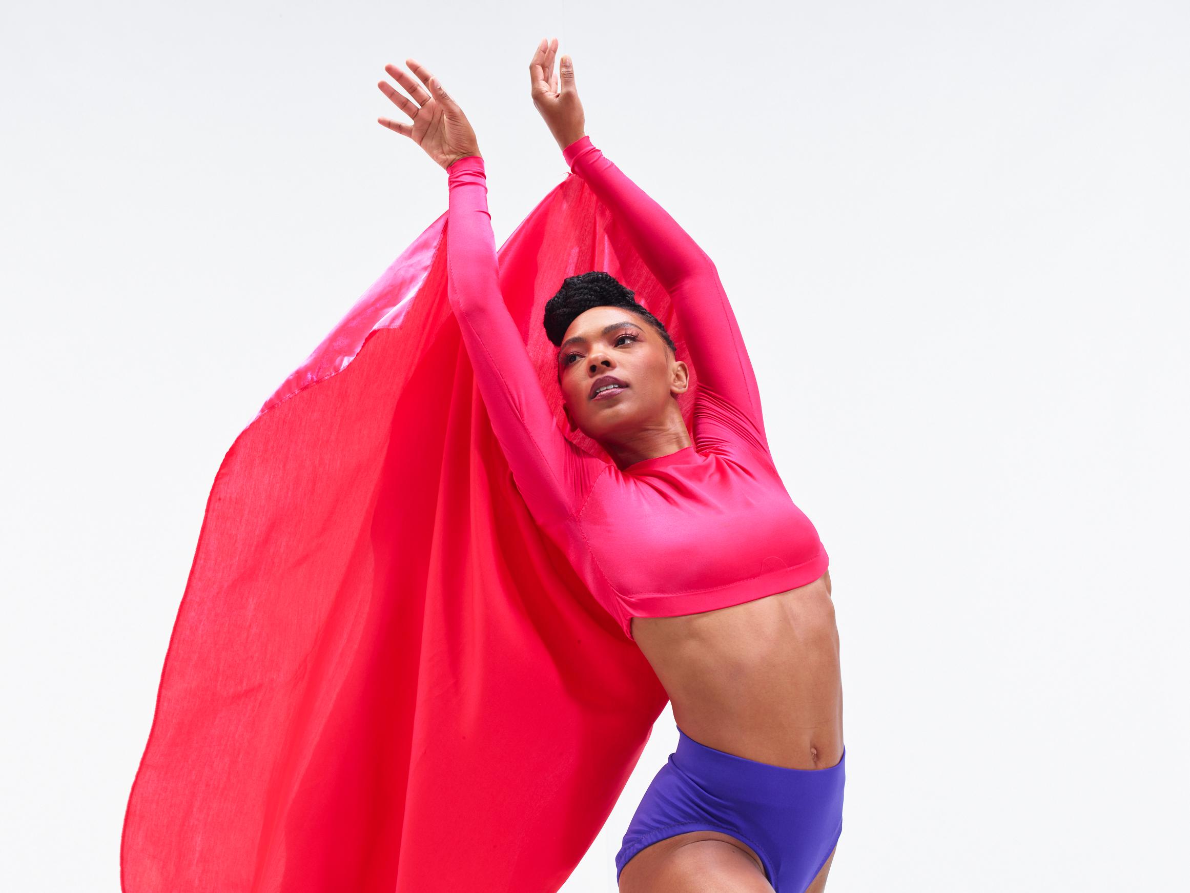 A woman in a hot pink long sleeve shirt looks up with pink fabric billowing behind her.