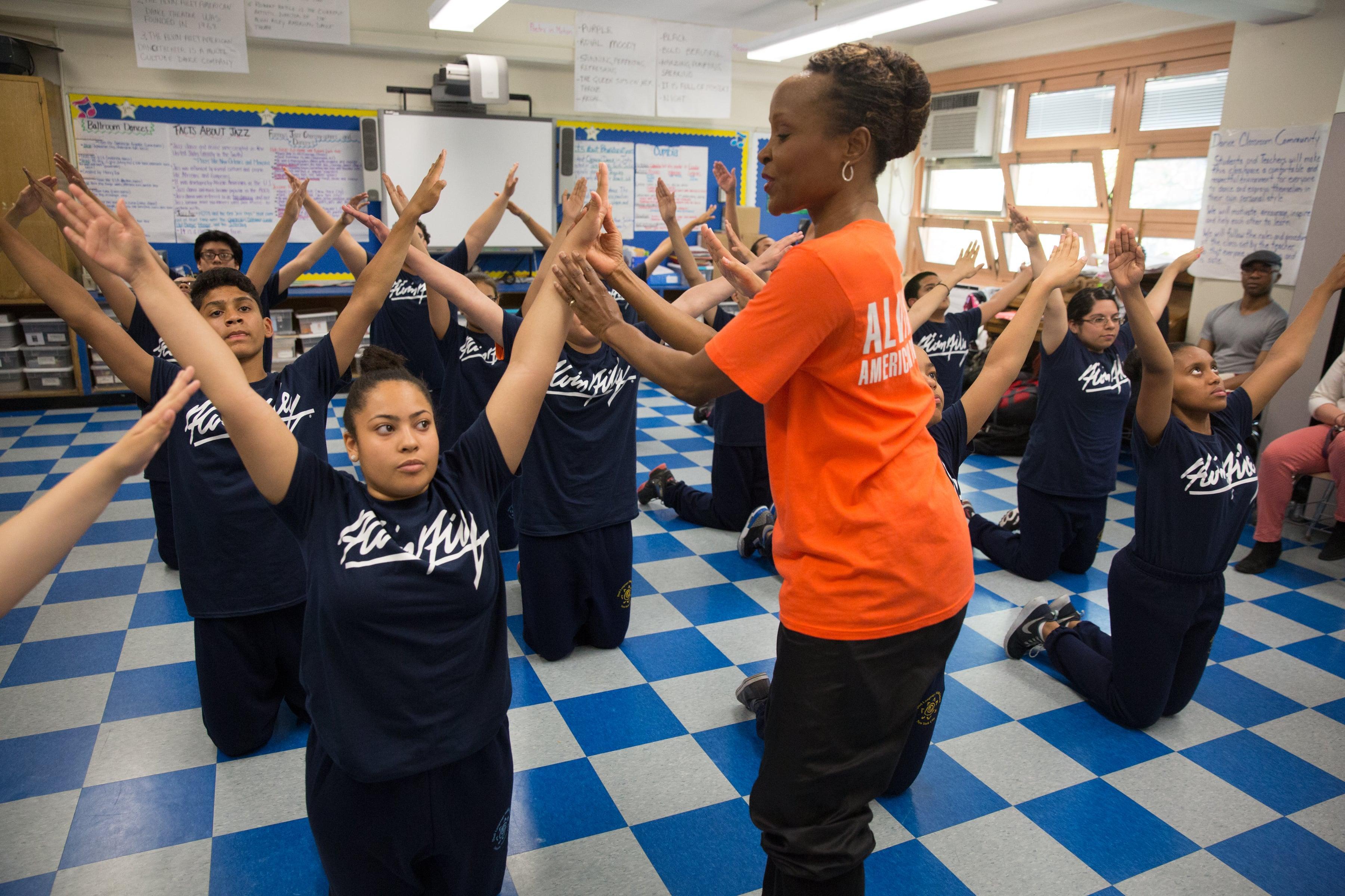 A teacher instructing students to raise their arms up