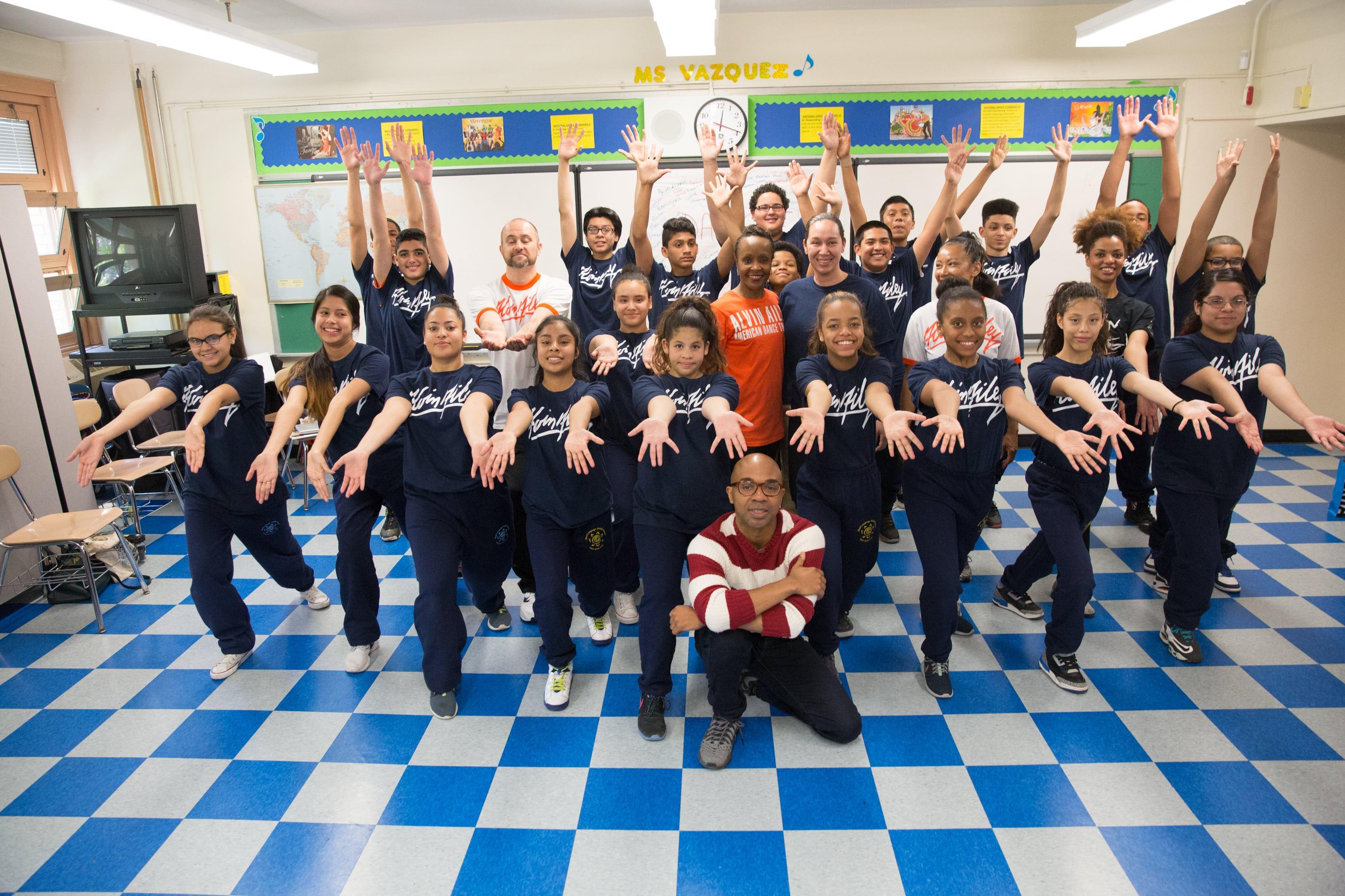 The students and teacher facing the camera and reaching their arms out