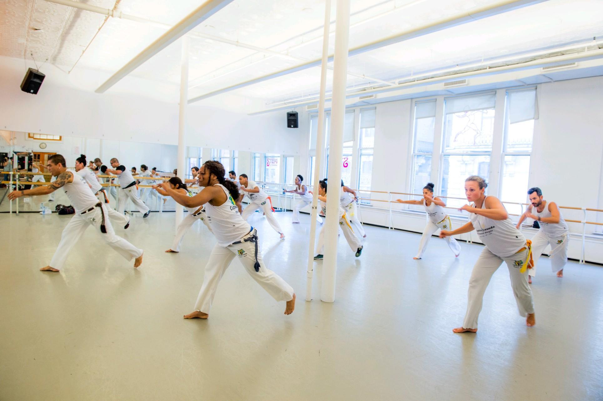 A bunch of students in all white outfits doing Capoeira in a studio