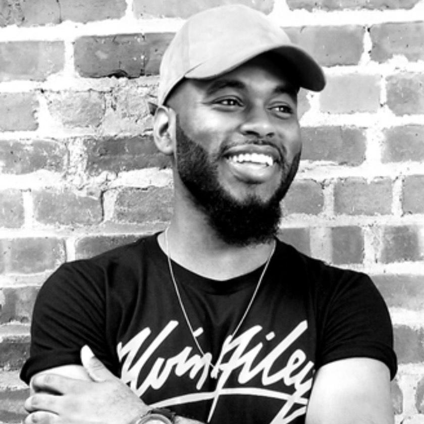 A black & white headshot on a brick wall