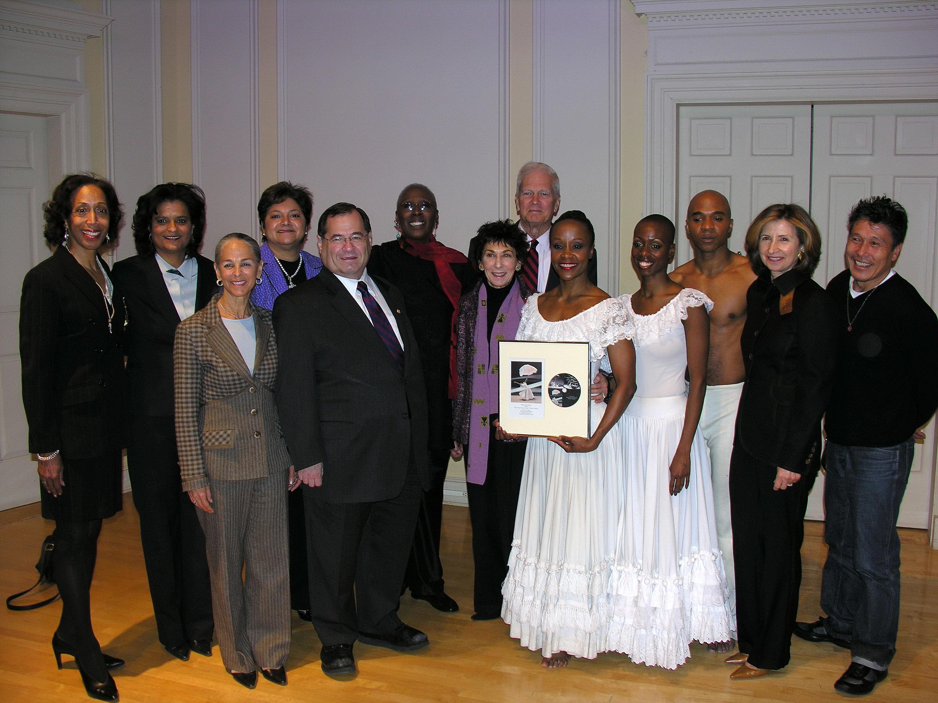 Group photo at the Library of Congress Ailey Archive Dedication Event, February 8, 2006. Individuals include members of the Alvin Ailey American Dance Theater, politicians, and guests. Two dancers in white costumes hold a framed photo. 