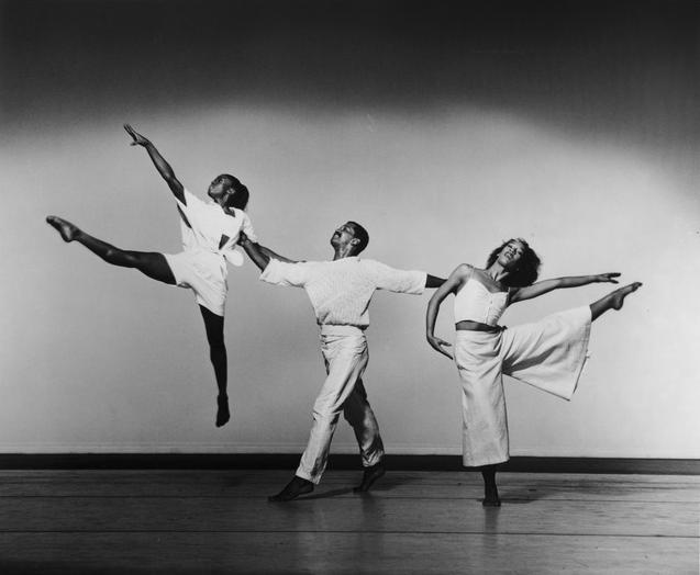 Black and white photo of Denise Jefferson with students from The Ailey School. Jefferson is seated in the center, smiling, surrounded by students dressed in dance attire. The students are also smiling and looking at her. The setting appears to be a dance studio. Photo by Julie Lemberger, 1984.