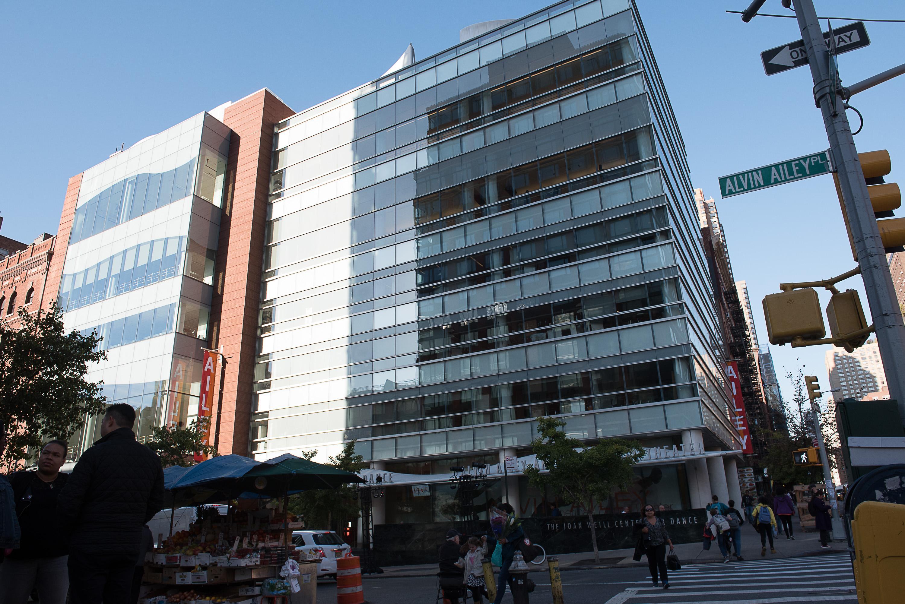 This image showcases The Joan Weill Center for Dance, a significant building for the Alvin Ailey American Dance Theater. Located at the corner of Alvin Ailey Place, the center is a modern, multi-story structure with a glass facade, reflecting the organization's commitment to transparency and openness. The building serves as the headquarters for the Alvin Ailey American Dance Theater and is a hub for dance education, rehearsal, and performance. The photograph, taken by Christopher Duggan in 2017, captures th