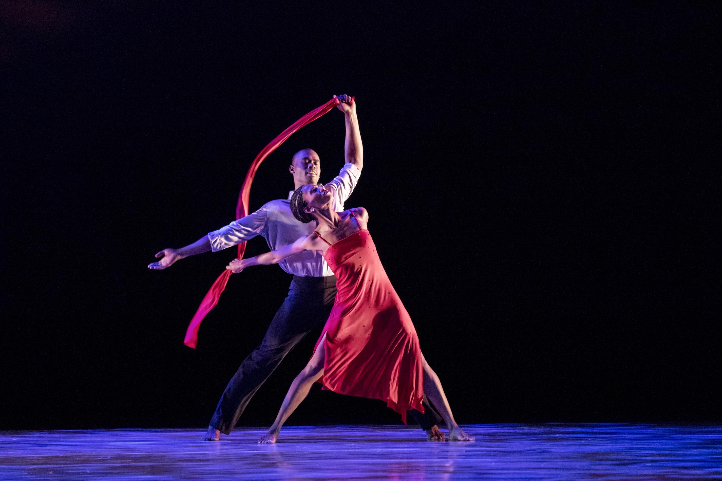 Two dancers looking up holding a long piece of fabric in the air