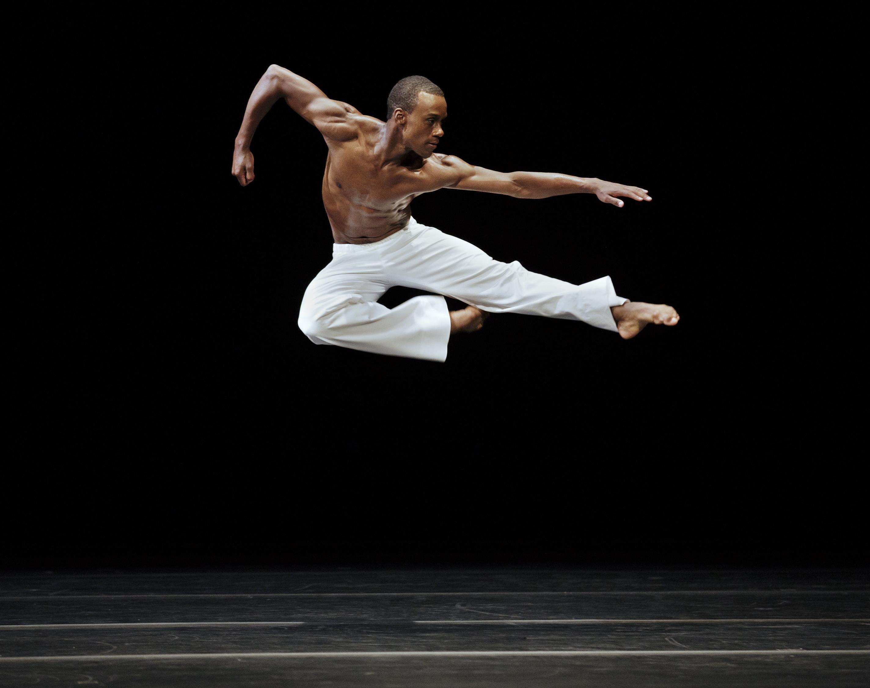 Shirtless dancer leaping in air with one leg bent