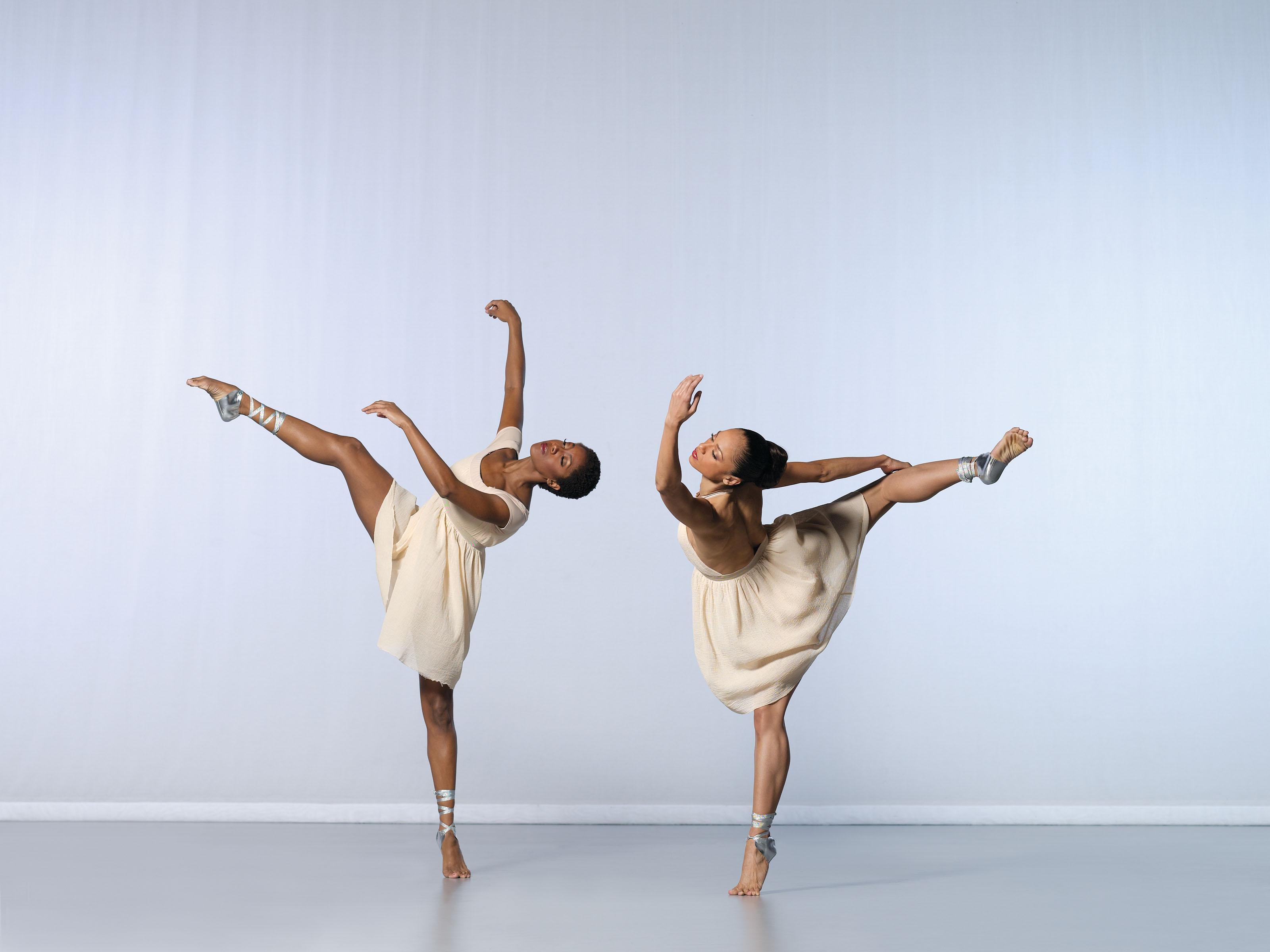 Two female dancers in dresses. One leaning forward and the other backwards with their leg in the air