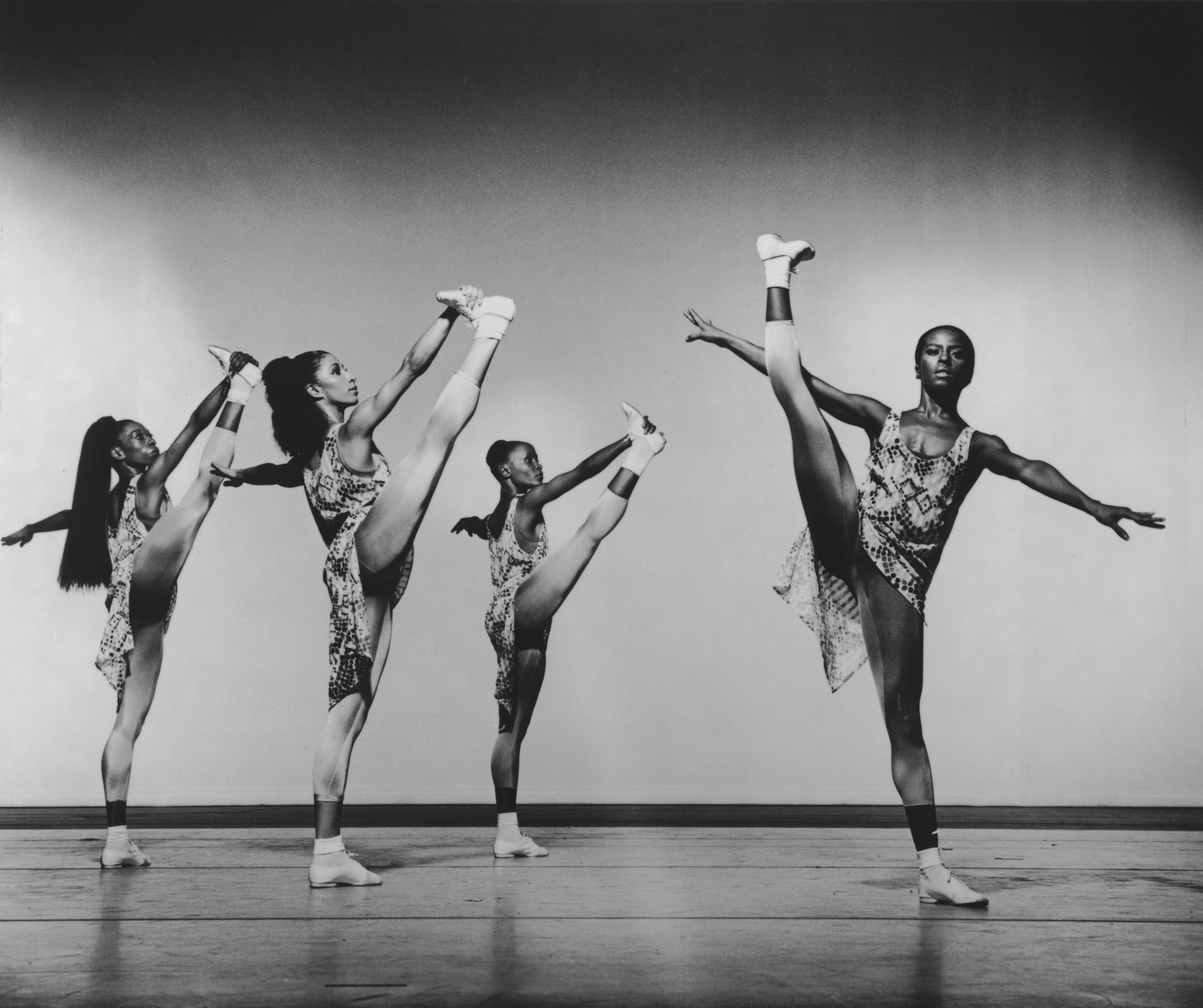 Black and white photo of Marilyn Banks, Neisha Folkes, Renee Robinson, and Deborah Manning performing in How to Walk an Elephant. All four dancers are in mid-pose with one leg raised high, wearing patterned leotards and socks.