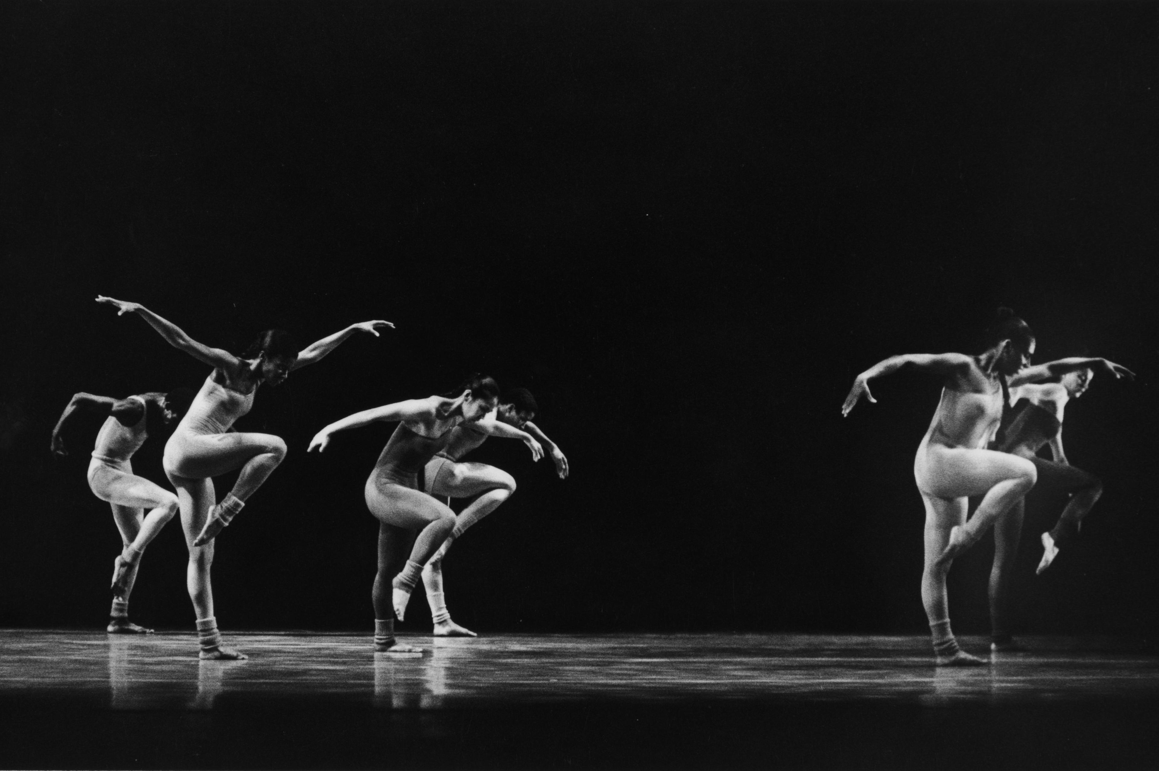 Black and white photo of five members of the company performing in Butterfly. They are in mid-movement, balancing on one leg with arms extended in various poses, wearing body-hugging costumes and socks.