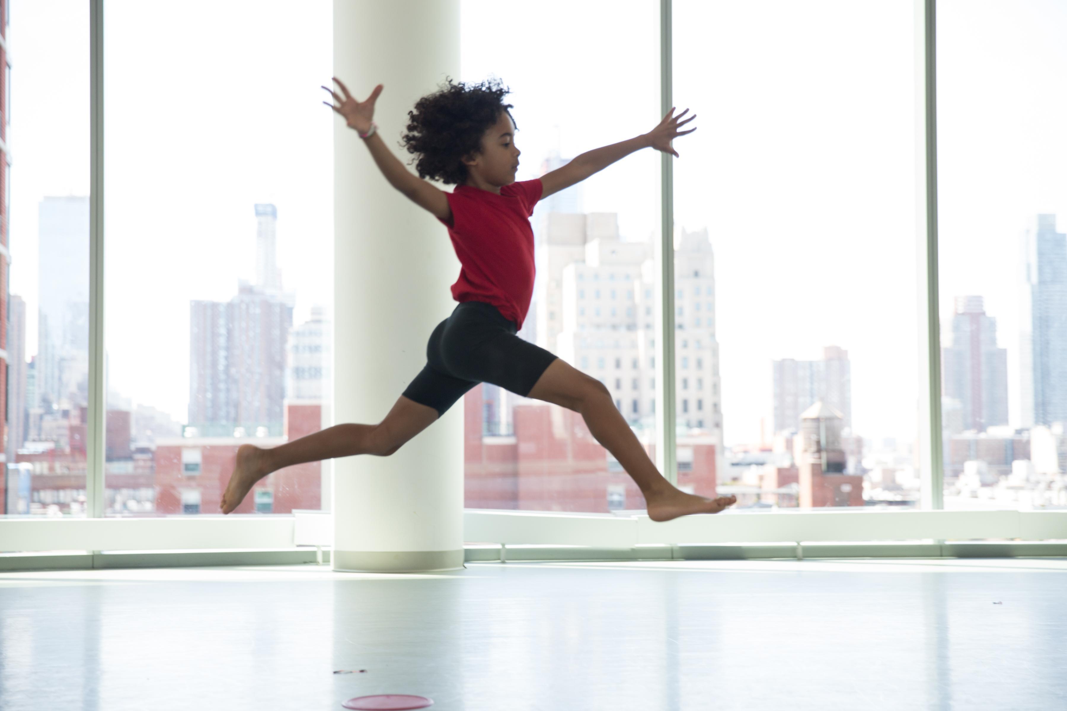  A boy in a red shirt and black shorts leaps in the air.