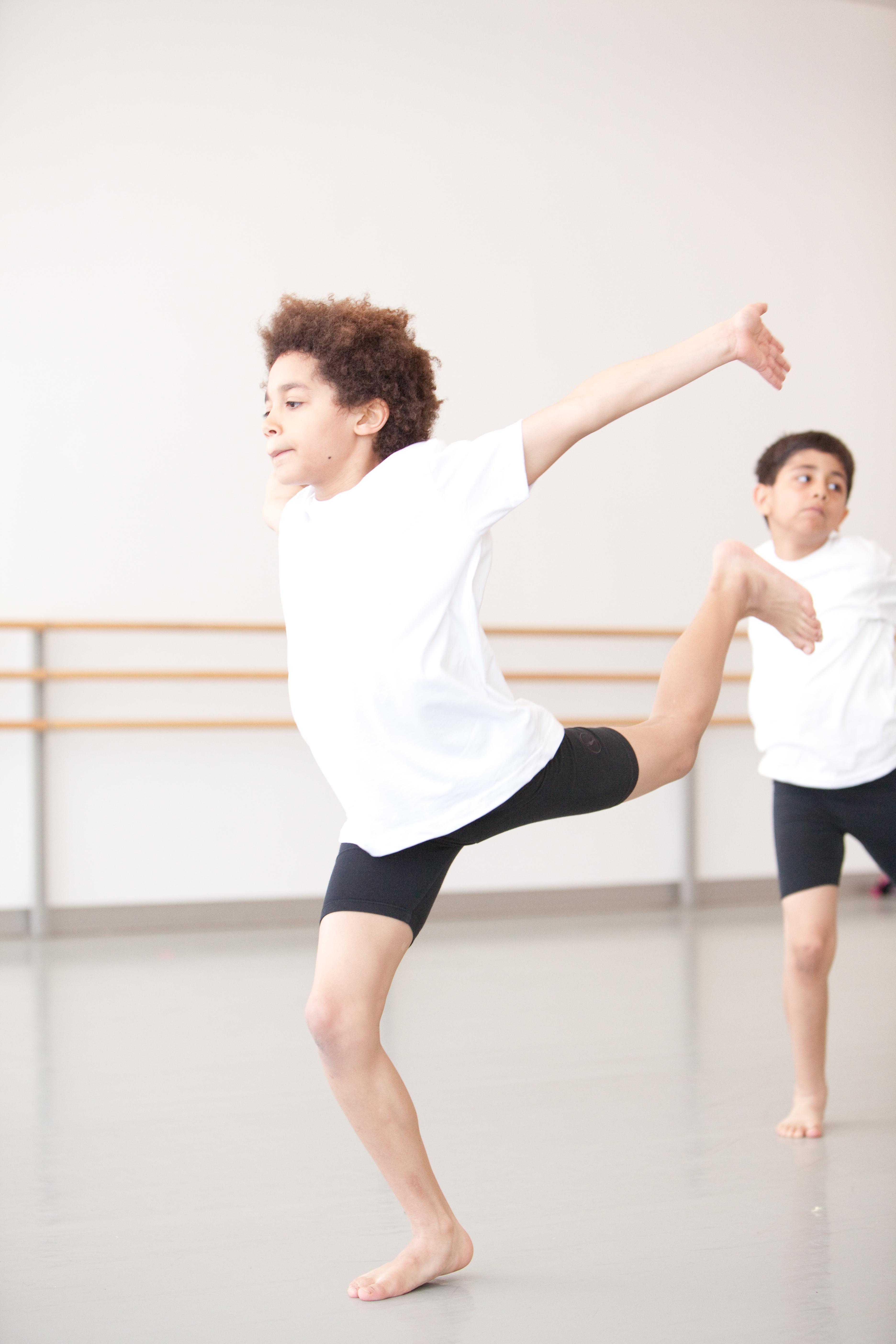 A boy dances in a studio. He appears to be jumping forward with his arms back.