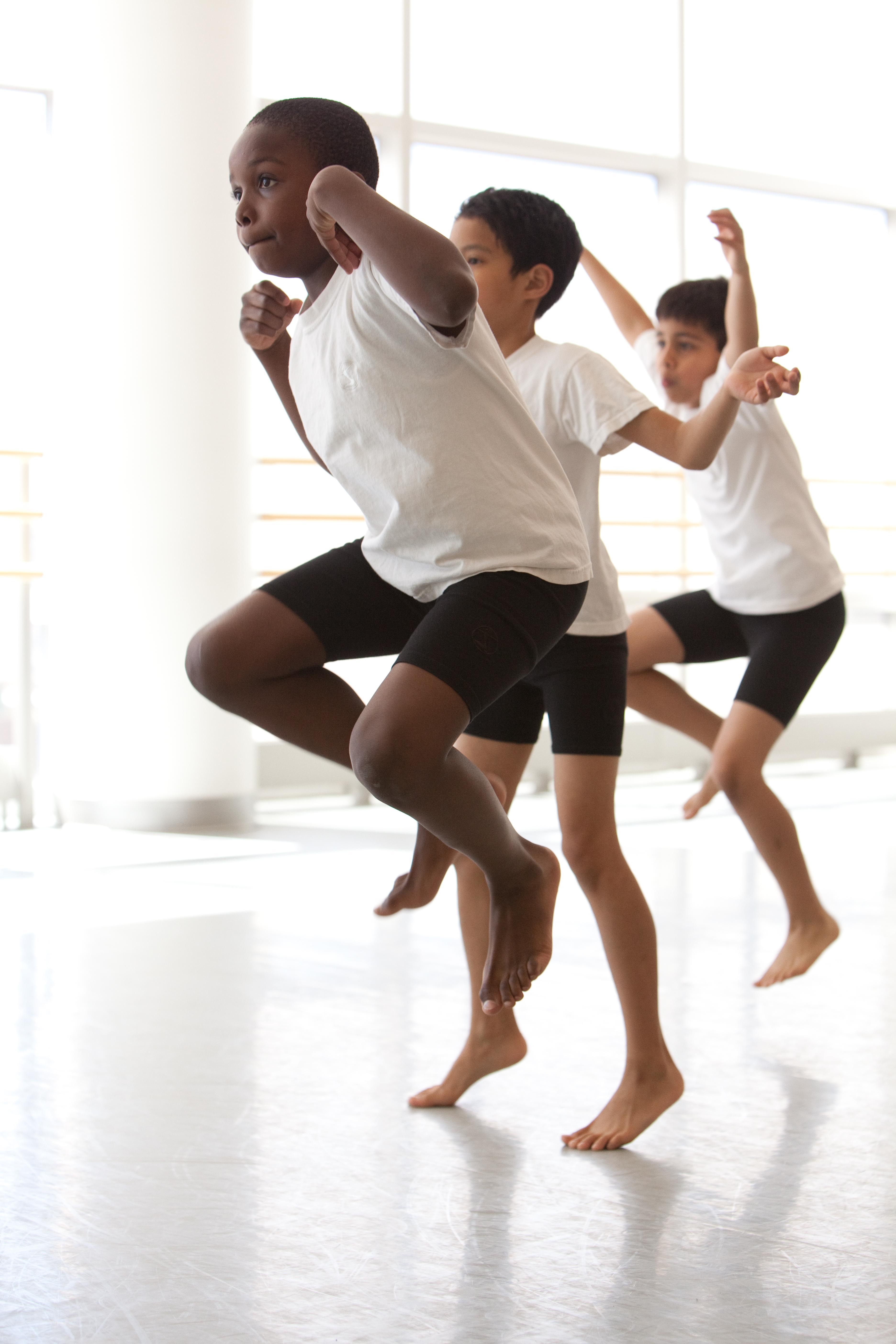 3 boys dance in a line. They have white tee shirts and black shorts on.