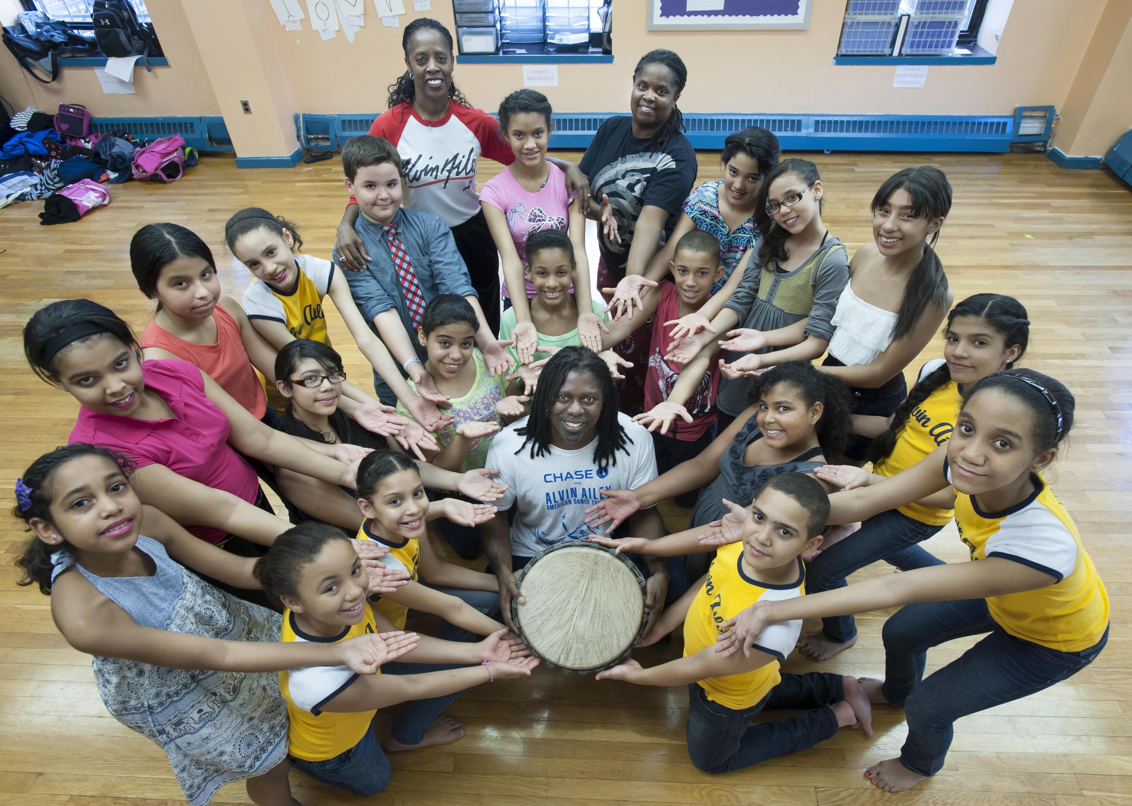 Group of young dancers surrounding AileyDance Kids instructors with all hands reaching toward a drum