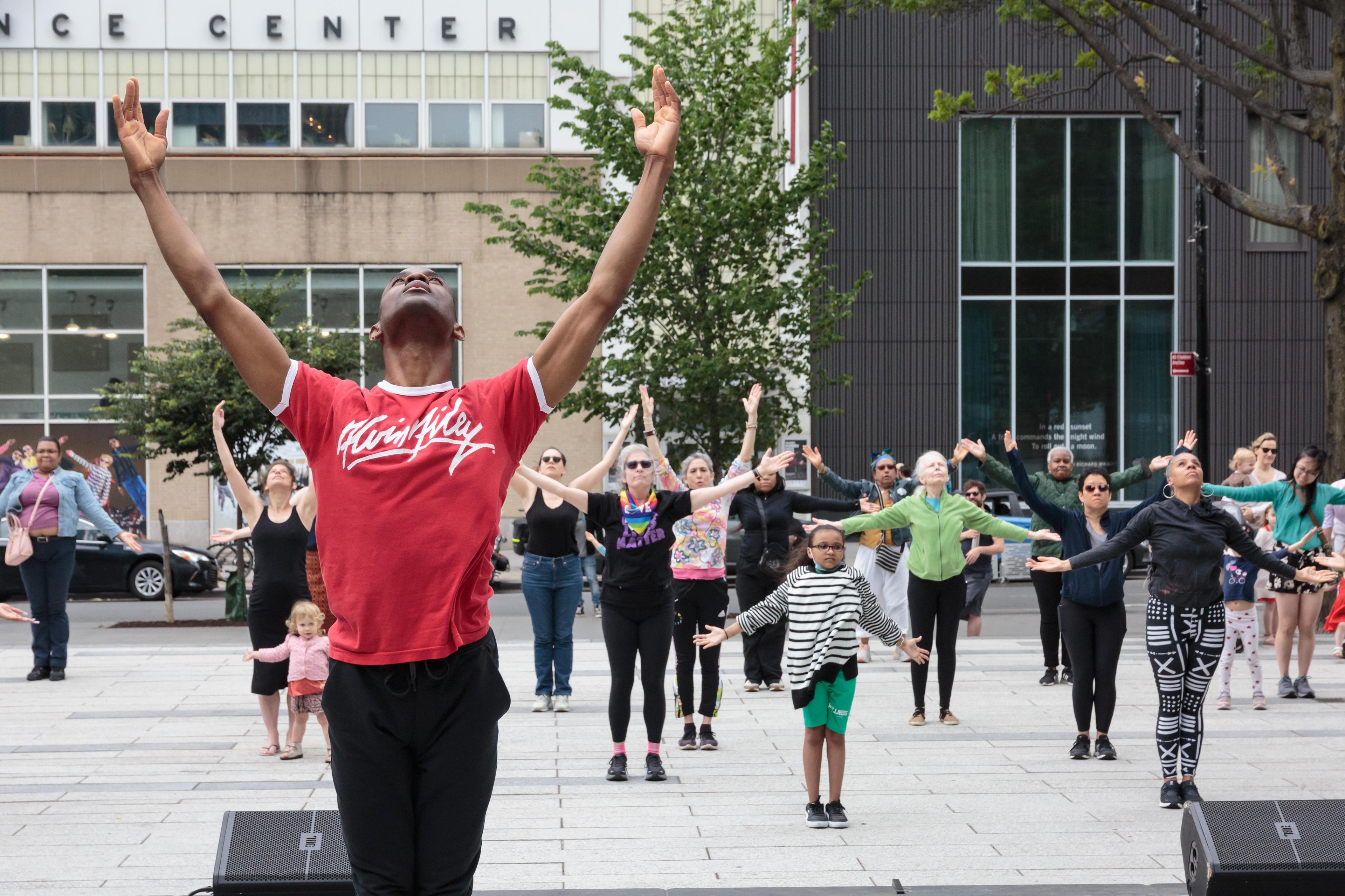 An instructor wearing an AILEY tshirt leading an all ages dance class outdoors