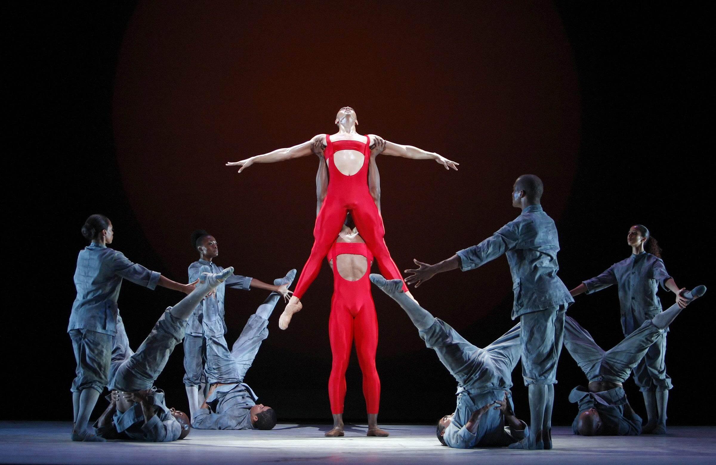 Two dancers in red surrounded by dancers in white. One of the dancers in red is holding up the other