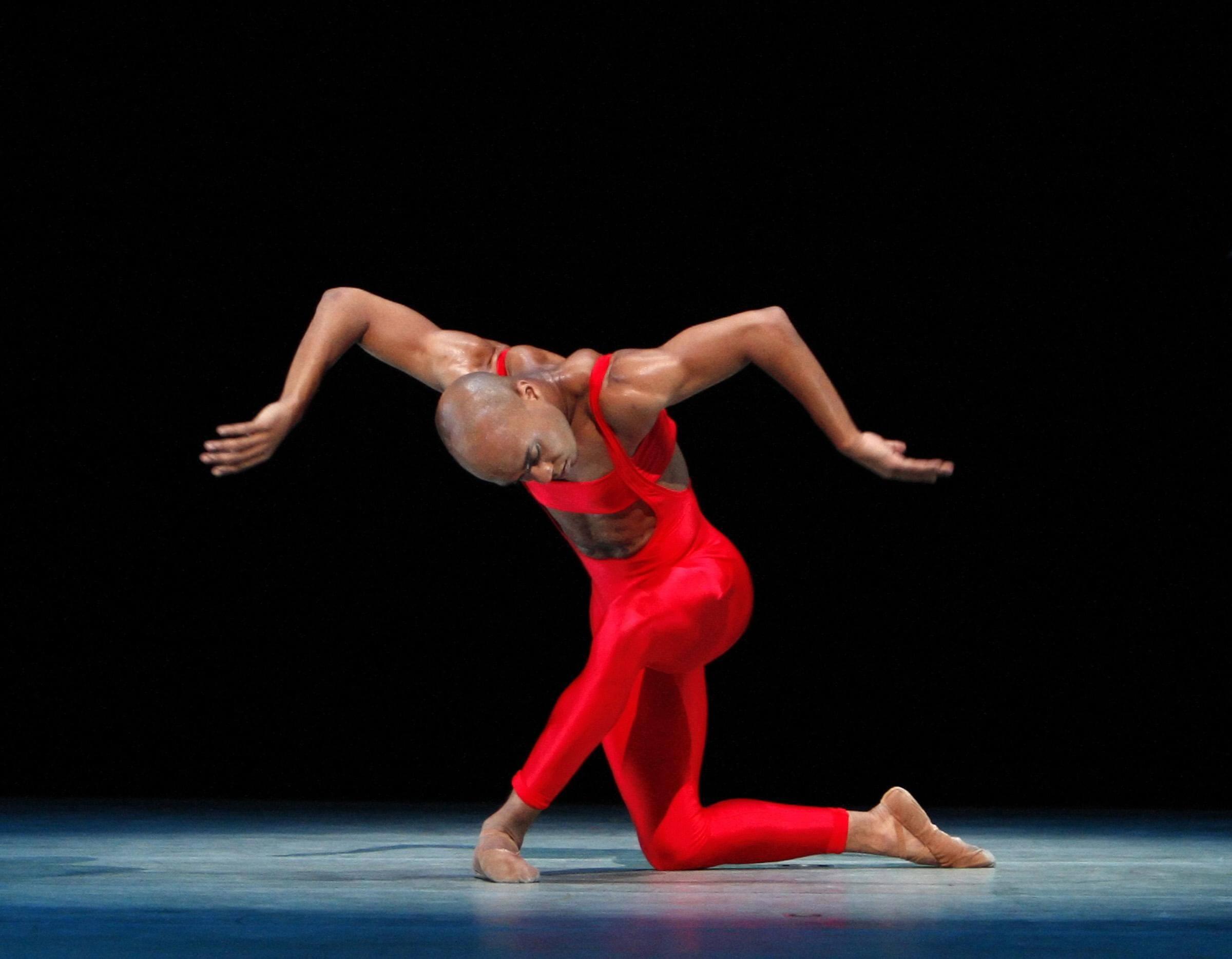 A dancer in red crouching down and holding their arms out like wings