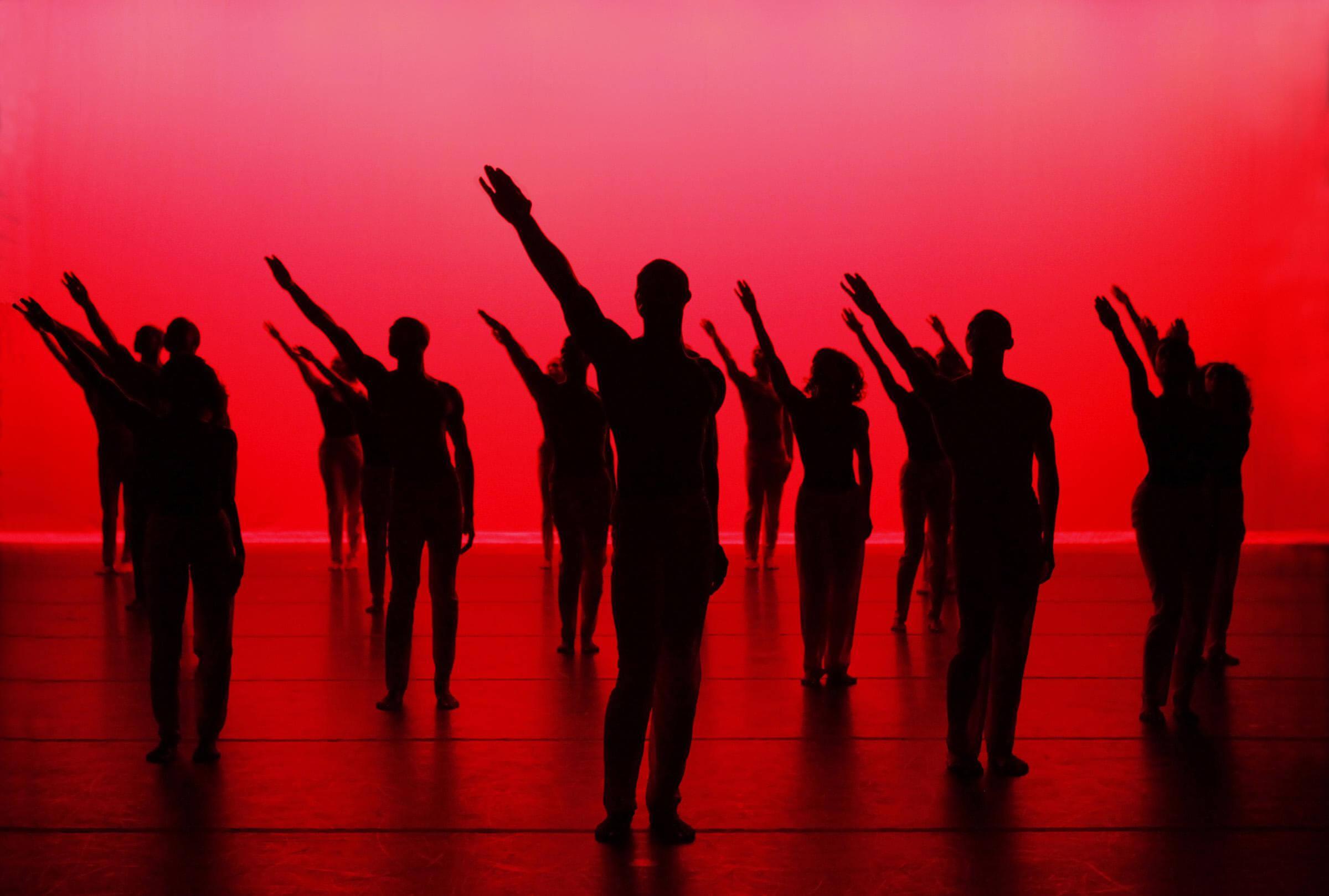 A large group of silhouettes extending their arms in the air