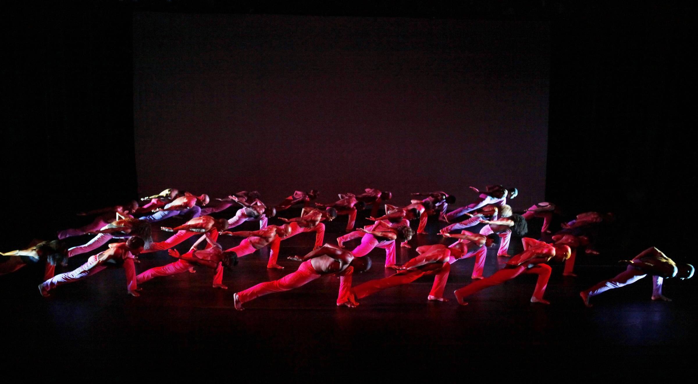 A large group of dancers all very low to the ground and facing their left