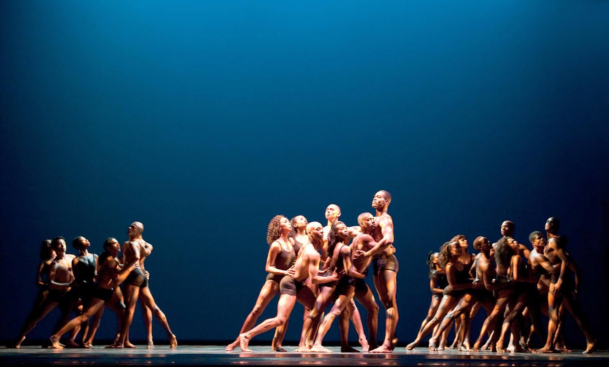 A group of dancers huddled together with the light focused on them. Two other groups are also close together, but not in the light