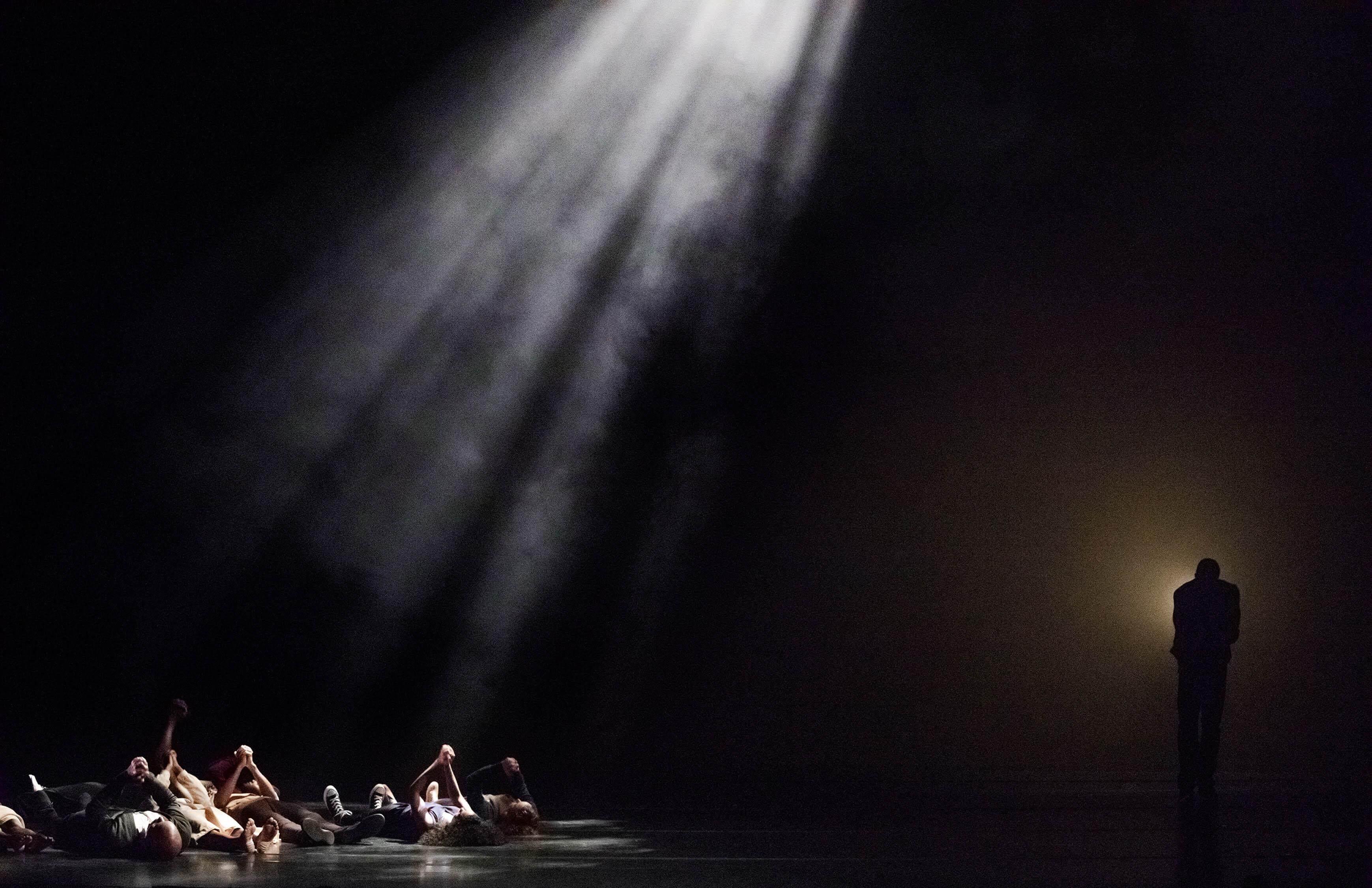 The spotlight shines on a bunch of dancers on the floor, Another light reveals the silhouette of the main dancer