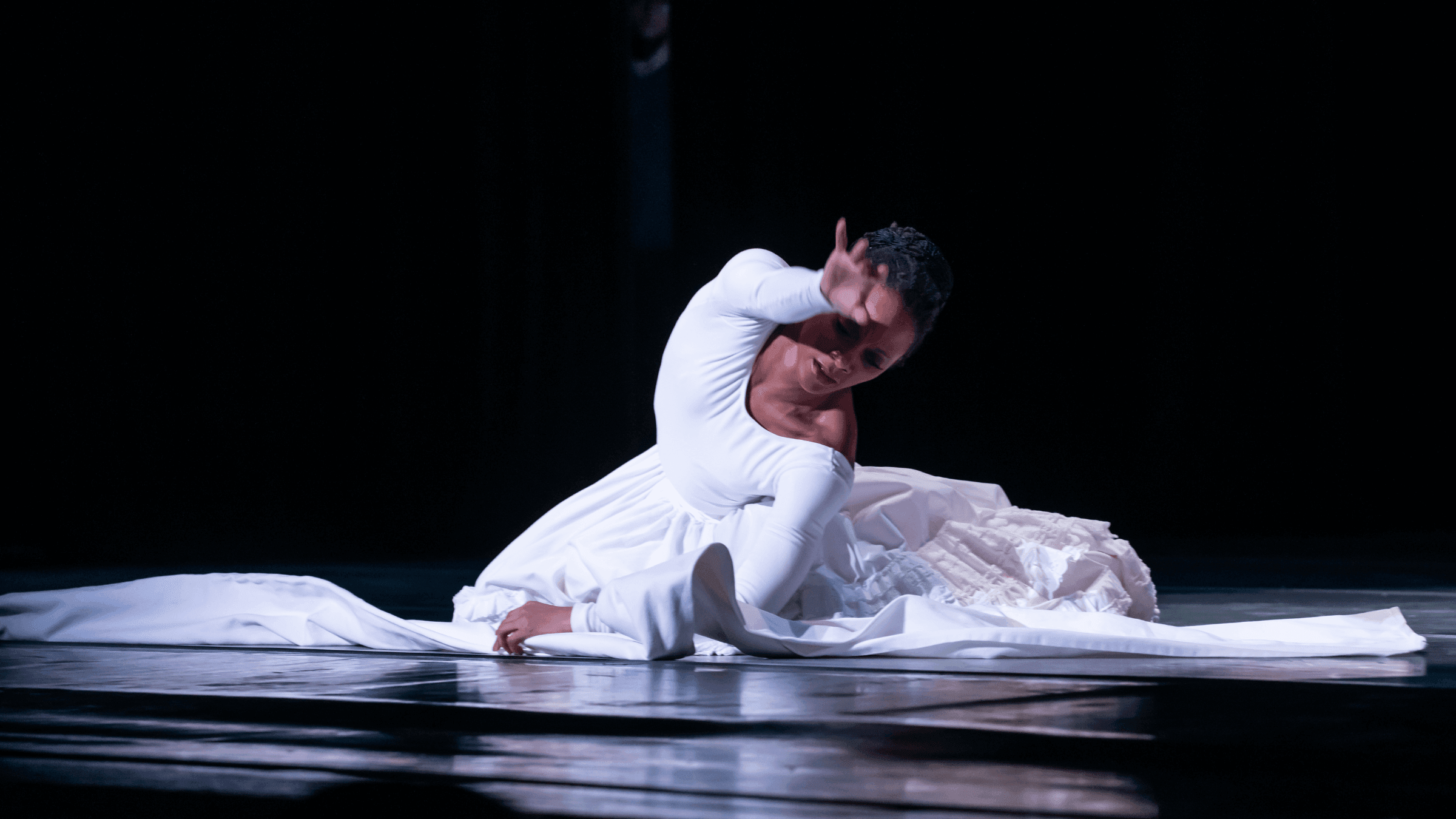 A woman in white sitting on stage reaching over her head