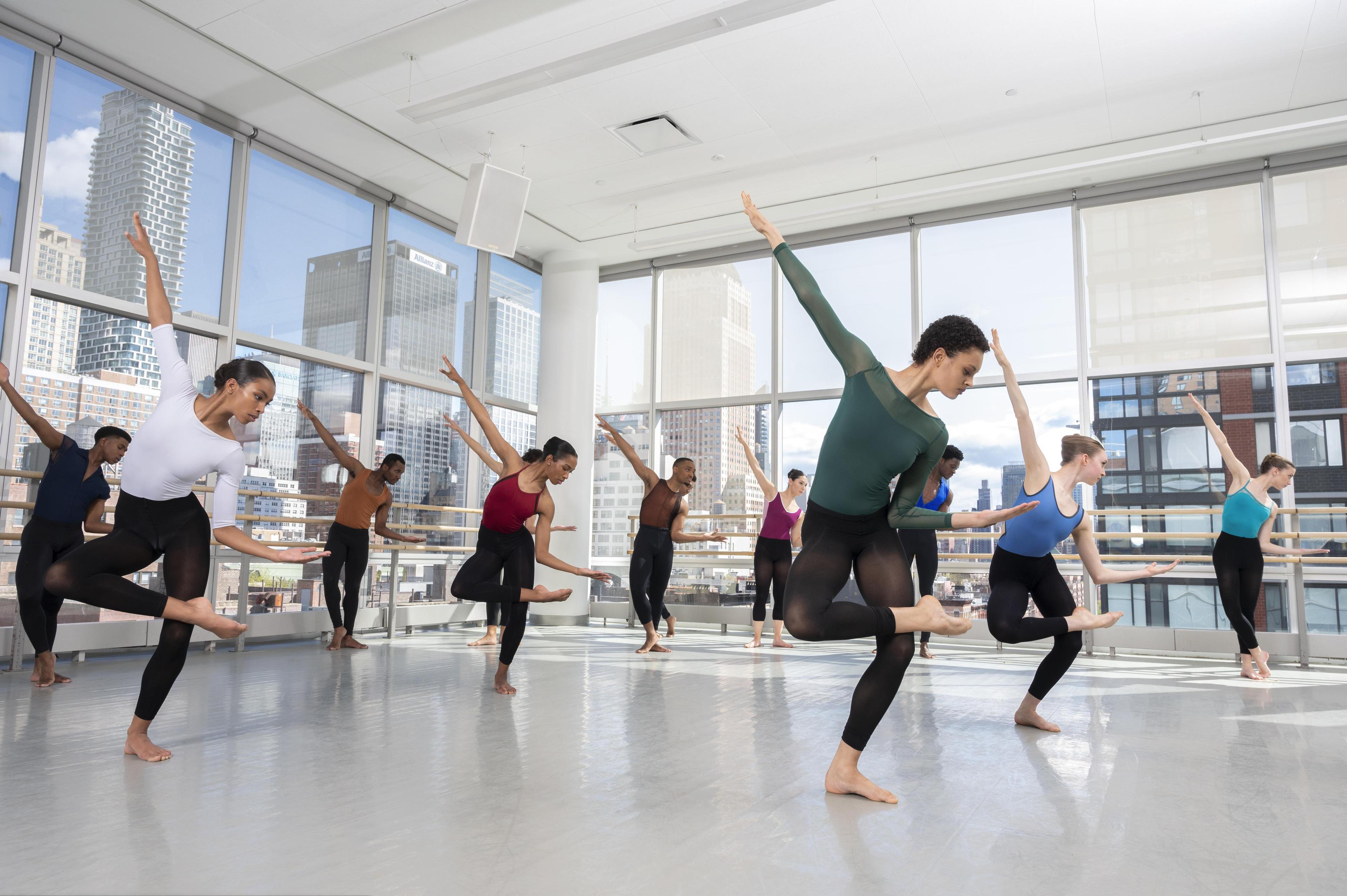 A classroom of dancer students with one leg in posse, one arm in the air, and the other close to their body 