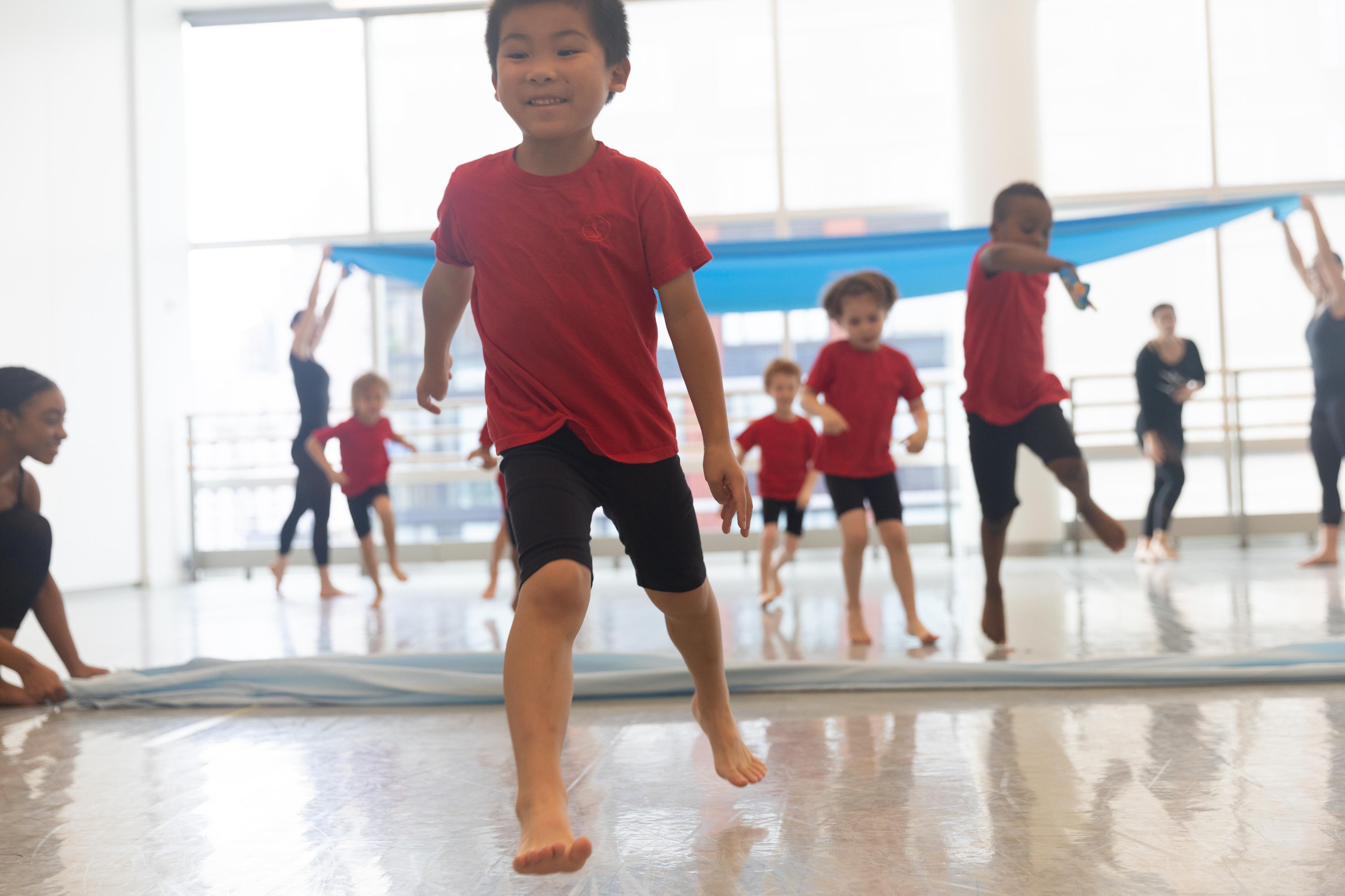 A group of boys in red t-shirts and black shorts jumping around in a dance studi