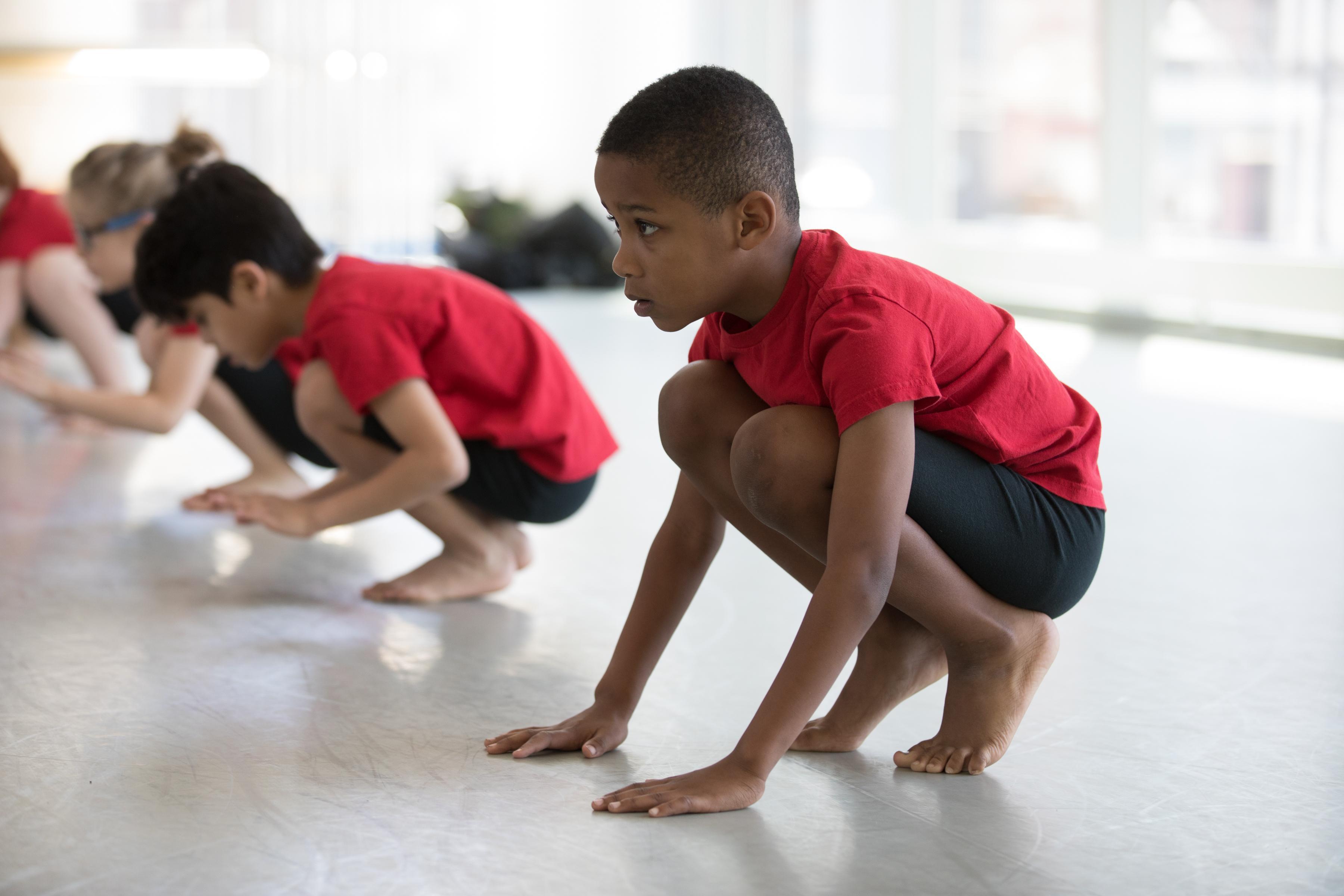 two boys in red t-shirts and black shorts crouch down on the ground.